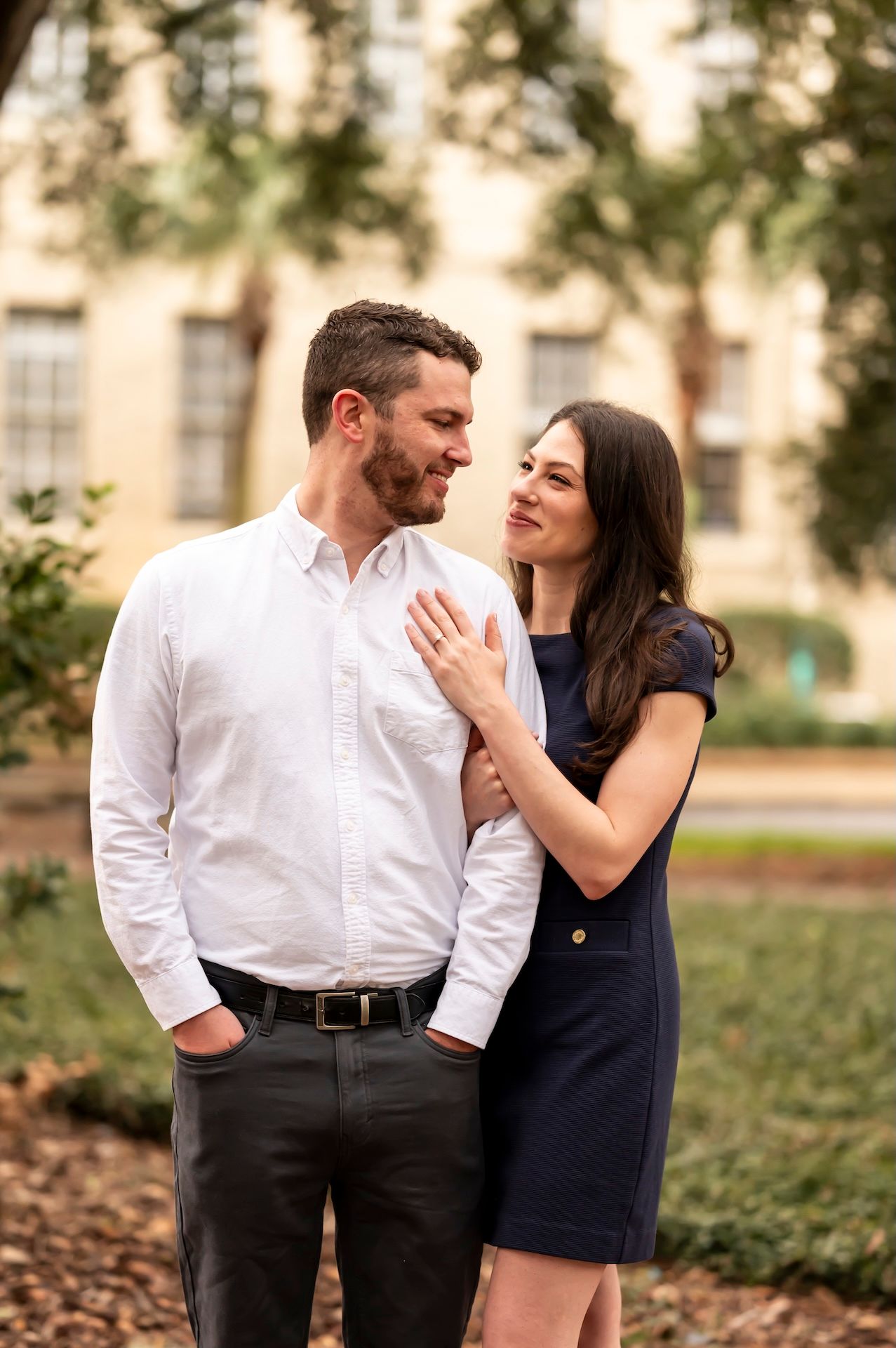 A couple shares a romantic moment in a garden setting during golden hour, wearing contrasting white and navy outfits.