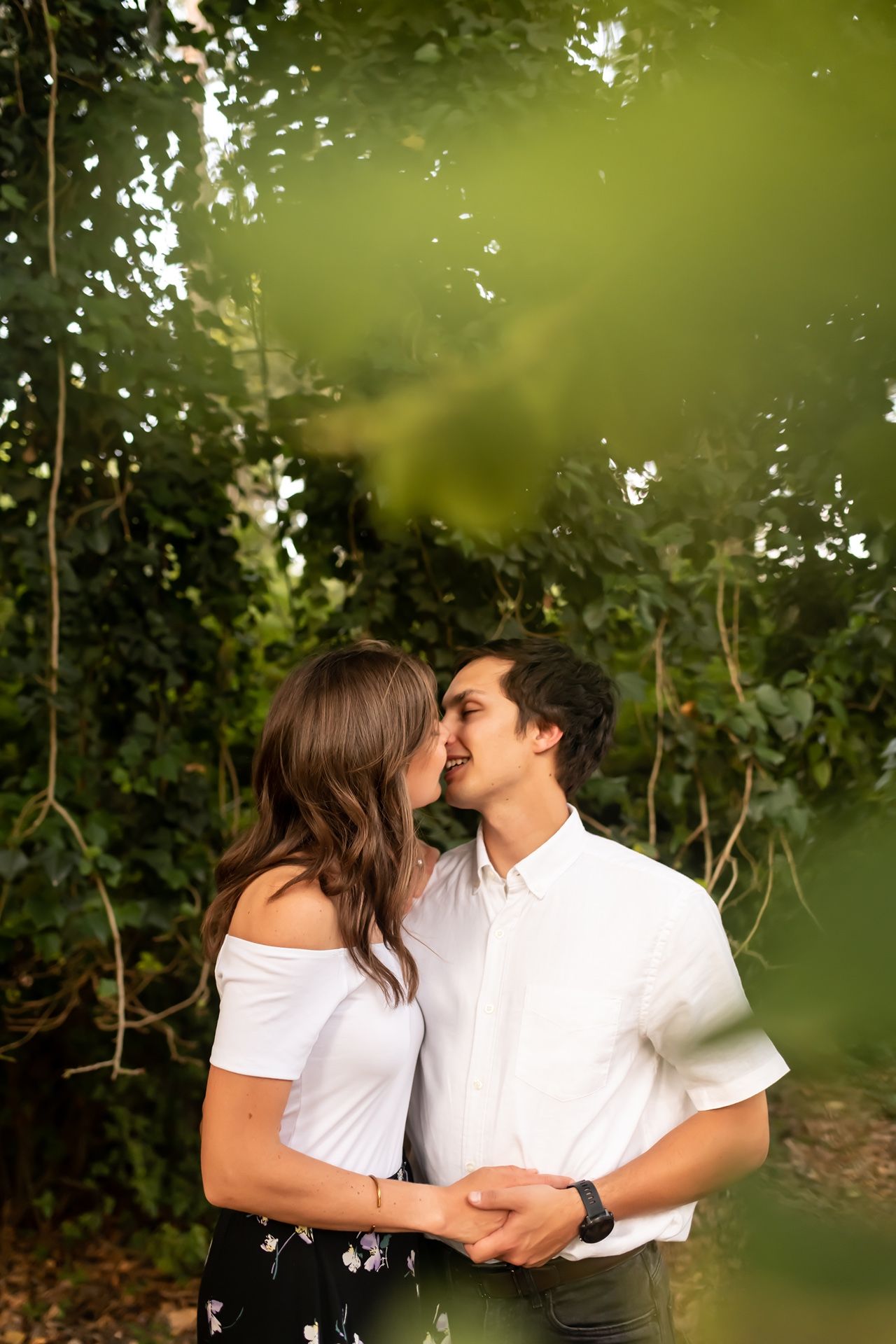 Romantic couple sharing a tender moment in a lush green garden setting with natural sunlight filtering through leaves.