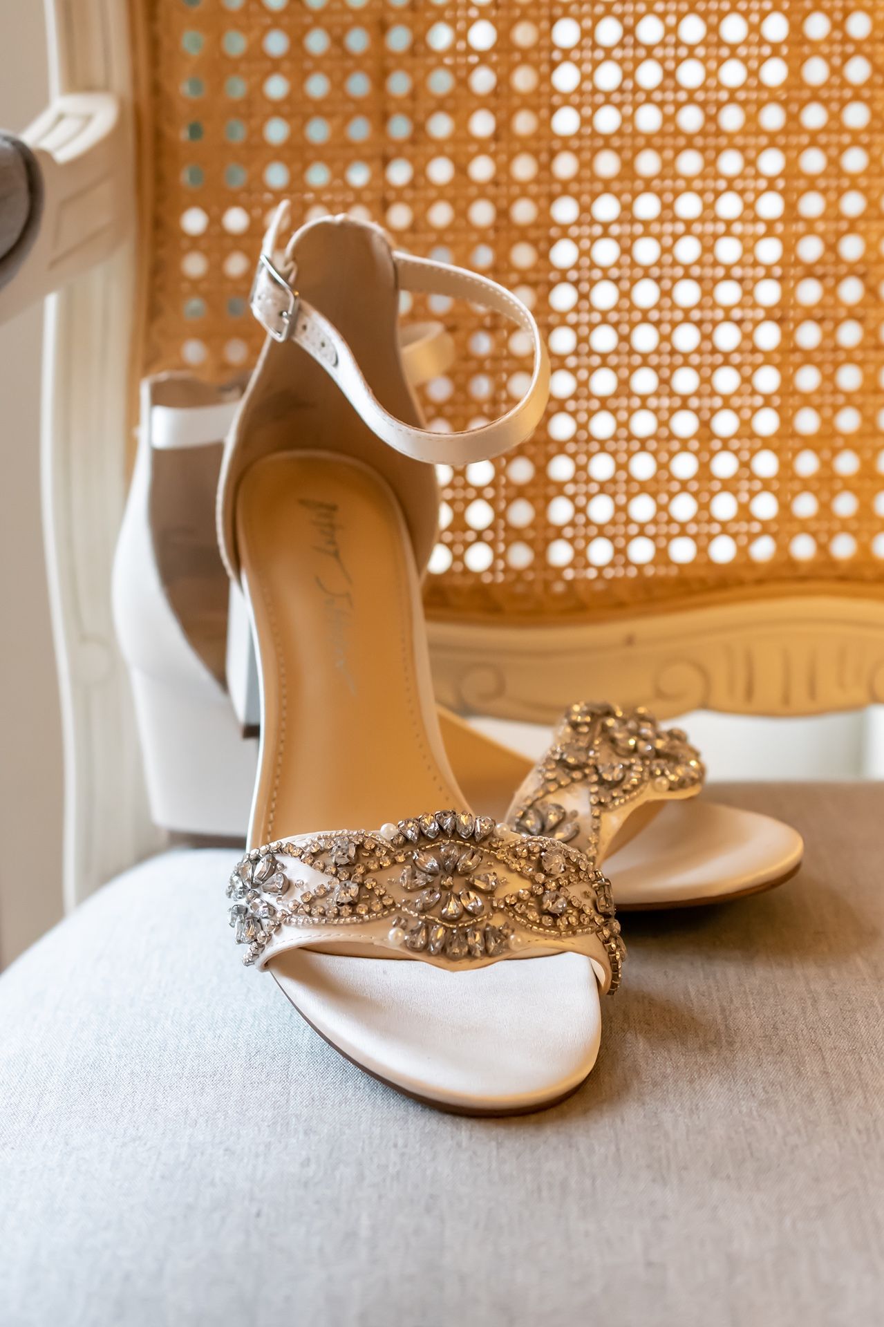 Elegant white wedding shoes with crystal embellishments displayed on a textured fabric.