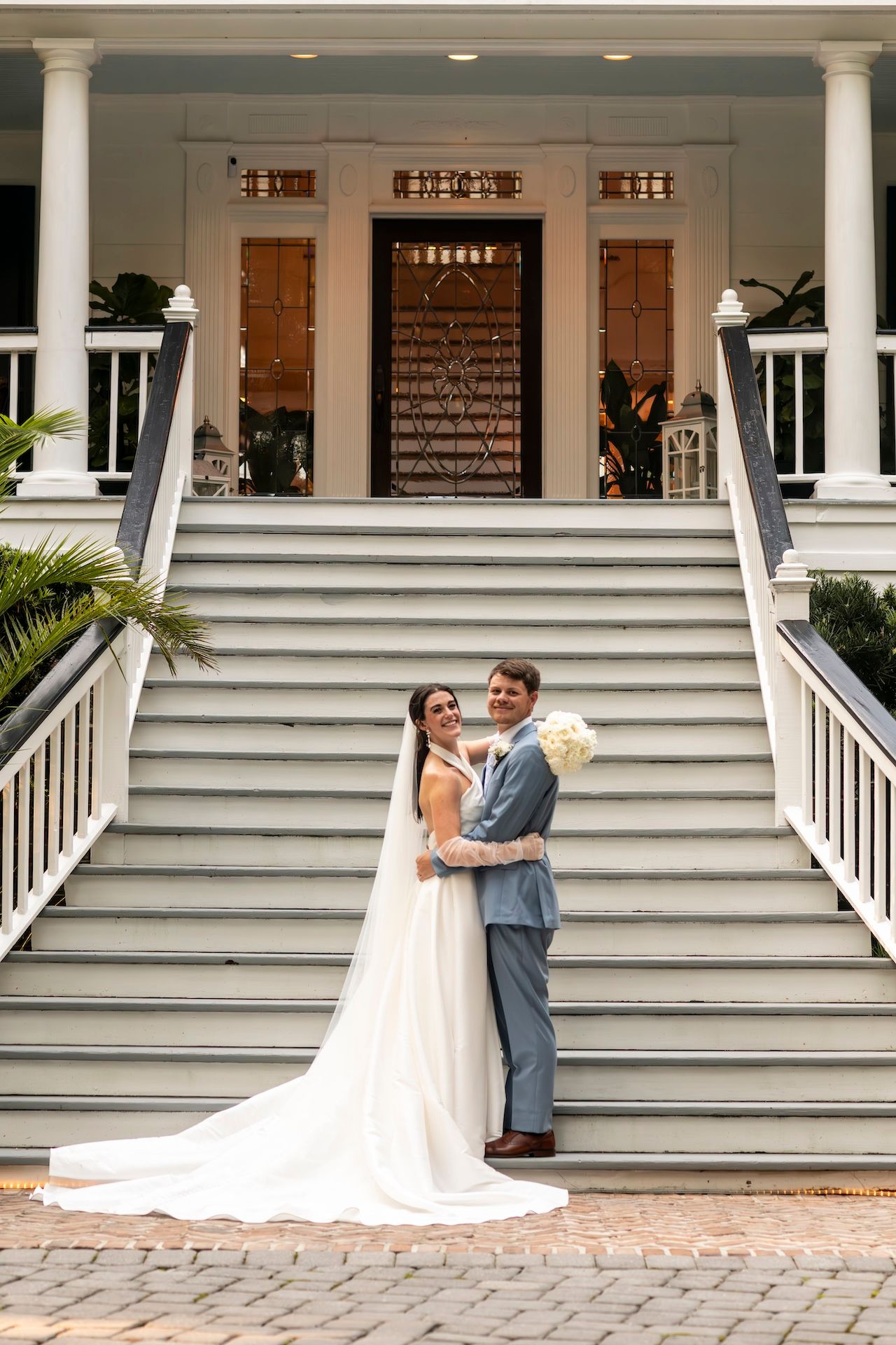 Newlyweds embrace on grand white steps of Southern plantation house with beautiful columned entrance.