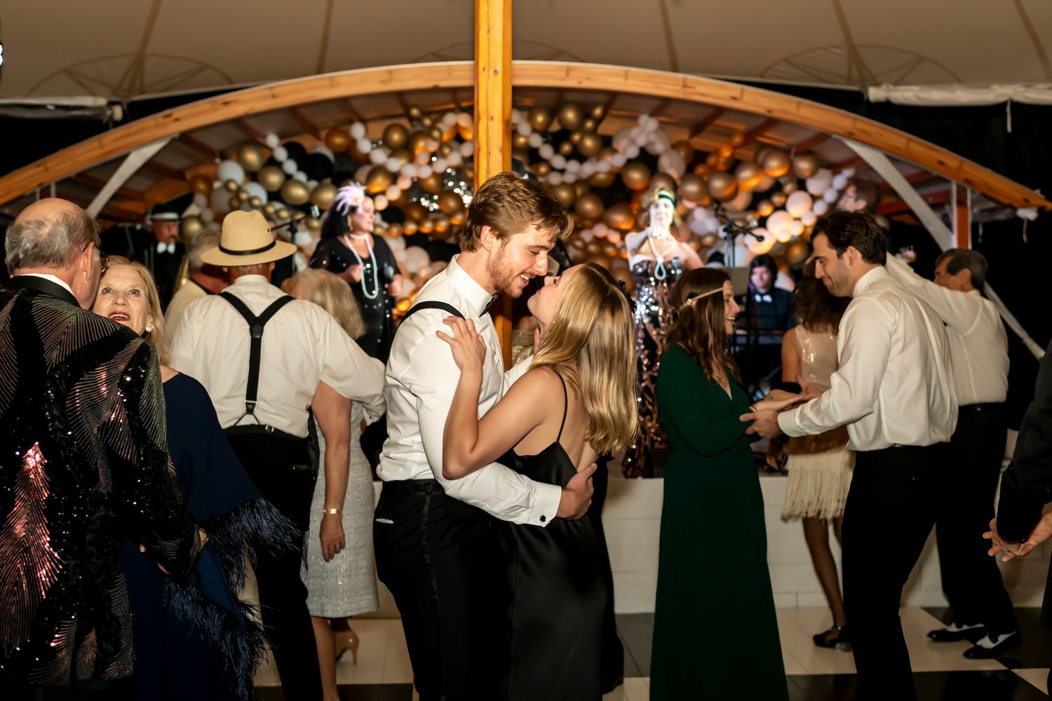 Couples dance under a wooden tent canopy at an elegant evening wedding reception with guests in formal attire.