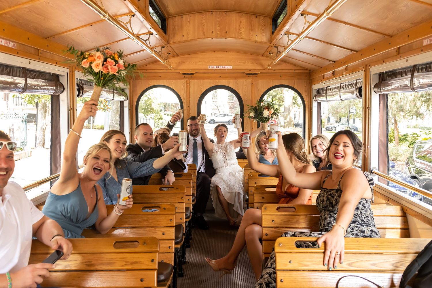 Interior view of a vintage wooden trolley or tour bus filled with happy passengers enjoying a sunny ride with arched windows.