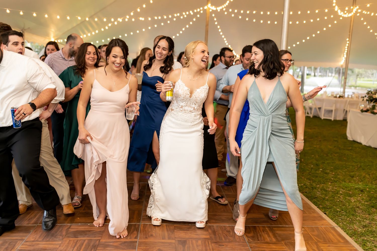 Wedding guests dance and celebrate together under twinkling string lights at an outdoor evening reception.