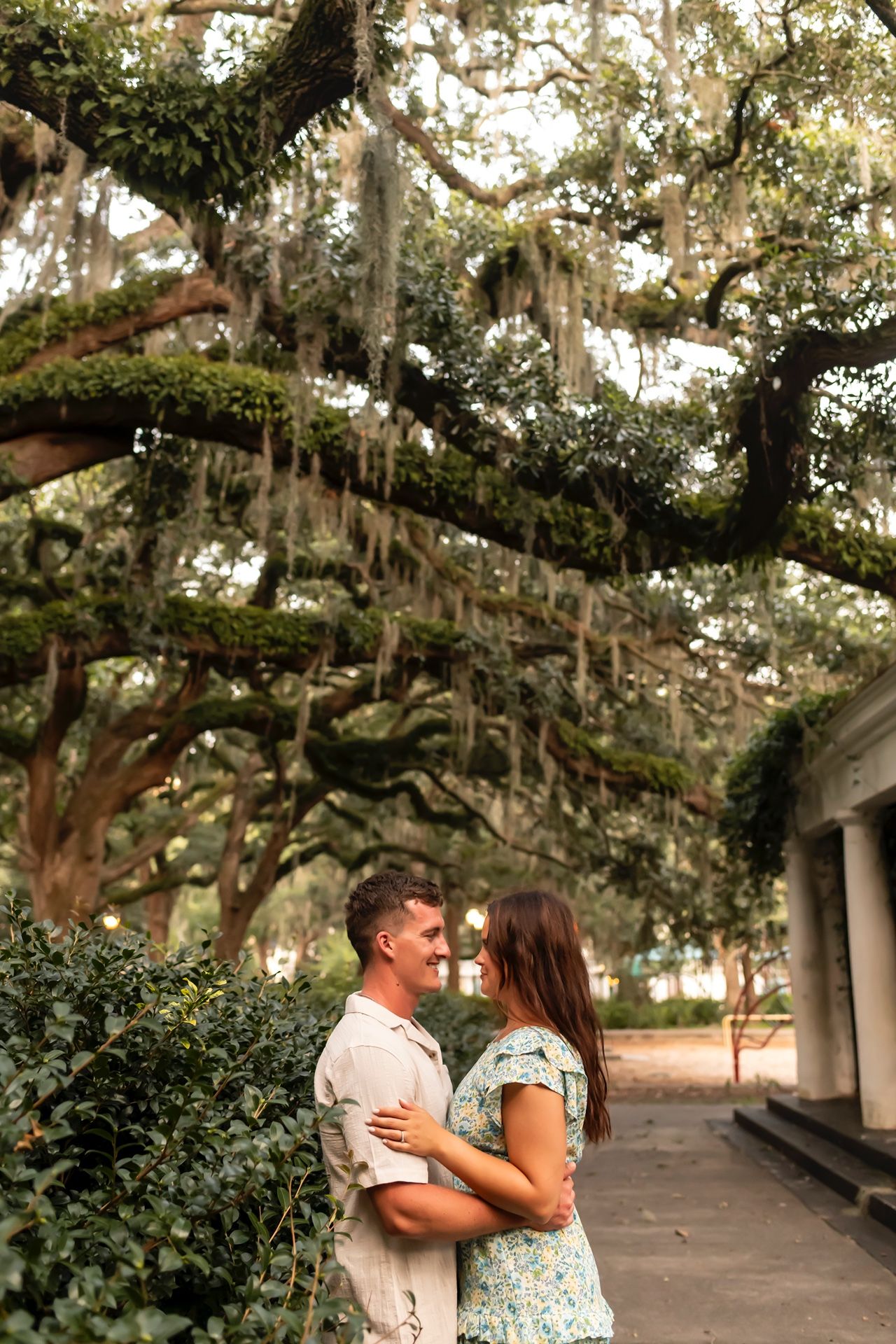 Couple embrace under Spanish moss draped oak trees on a walkway in a romantic Southern garden setting.
