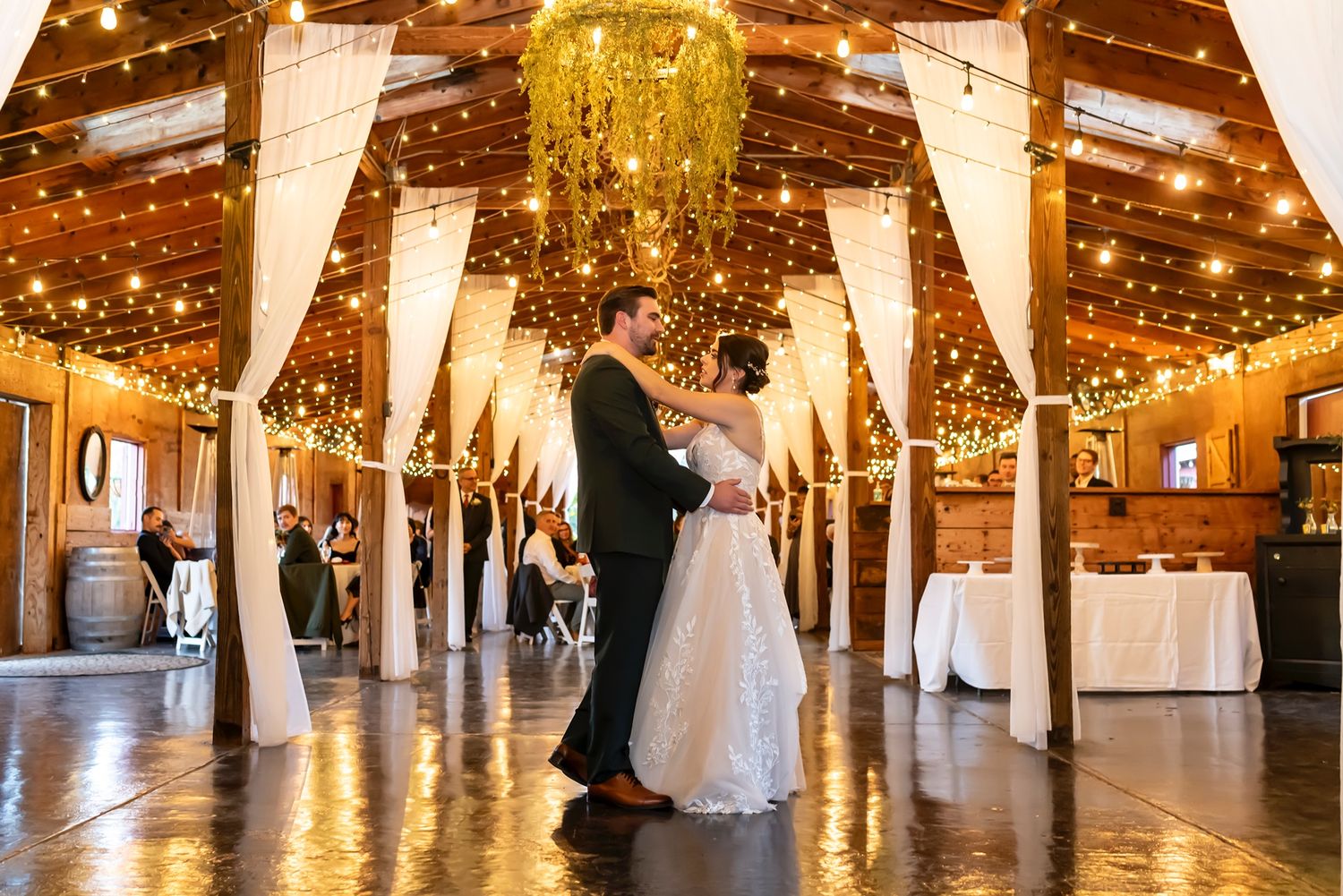 Reception hall decorated with elegant white drapes, golden fairy lights, and chandeliers for a romantic wedding celebration.