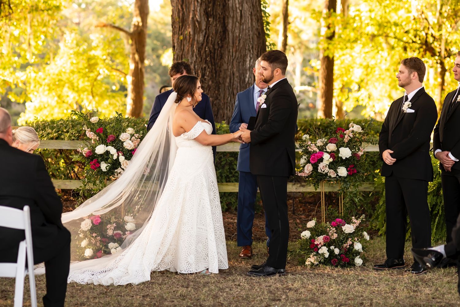 Elegant outdoor wedding ceremony in autumn with golden foliage and pink floral arrangements in a wooded setting.