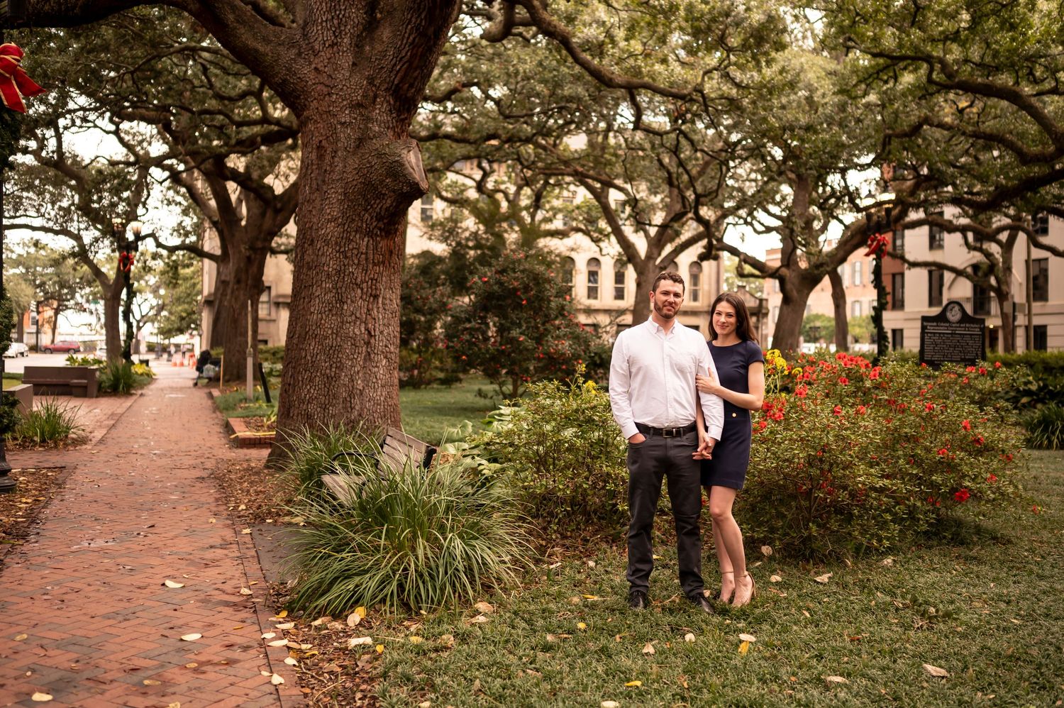A romantic engagement photo shoot under oak trees along a brick path lined with Spanish moss and landscaping.