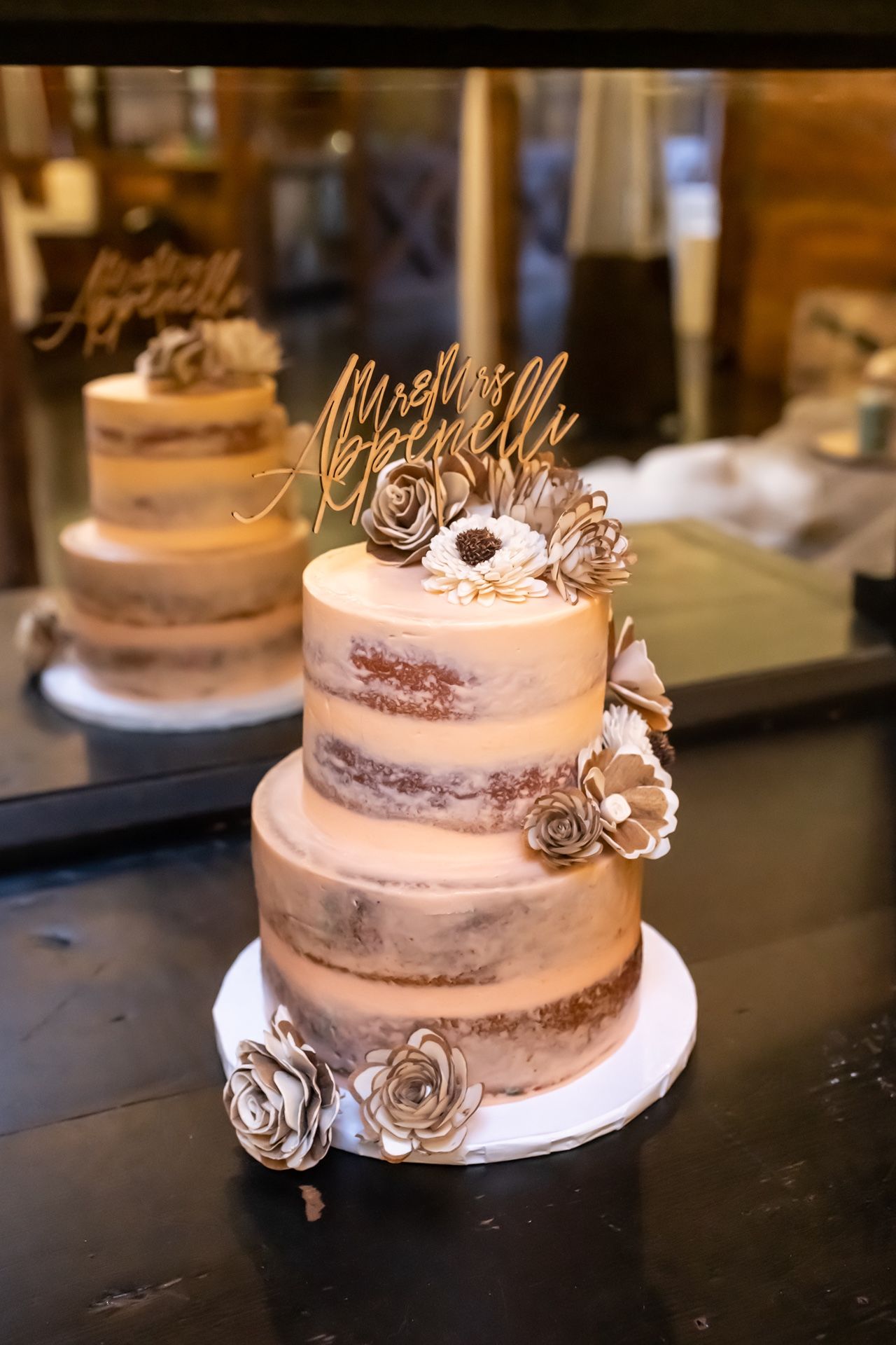 Semi-naked wedding cake with three tiers decorated with metallic roses and a cursive cake topper.