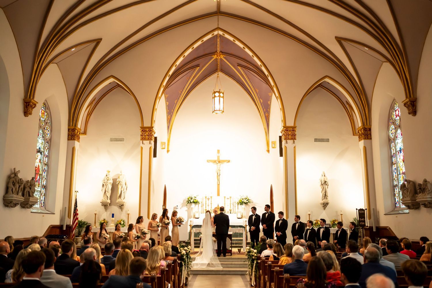 Interior view of a traditional church wedding ceremony with vaulted Gothic arches and a large crowd gathered in the pews.