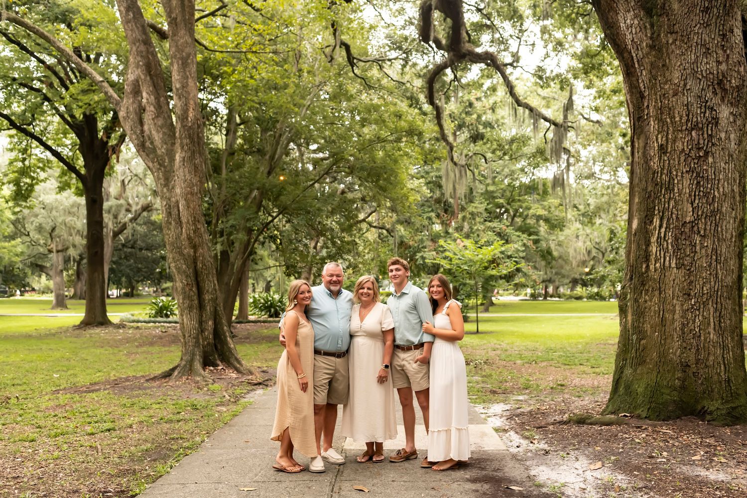 A family photoshoot taking place under large oak trees in a scenic park setting.