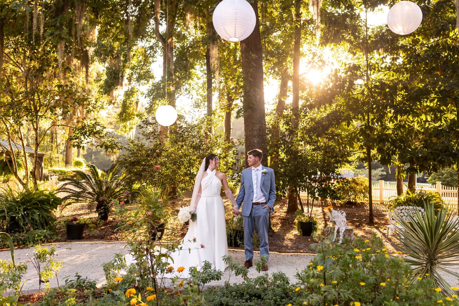 Romantic garden wedding celebration with paper lanterns hanging from trees at golden hour among lush greenery.