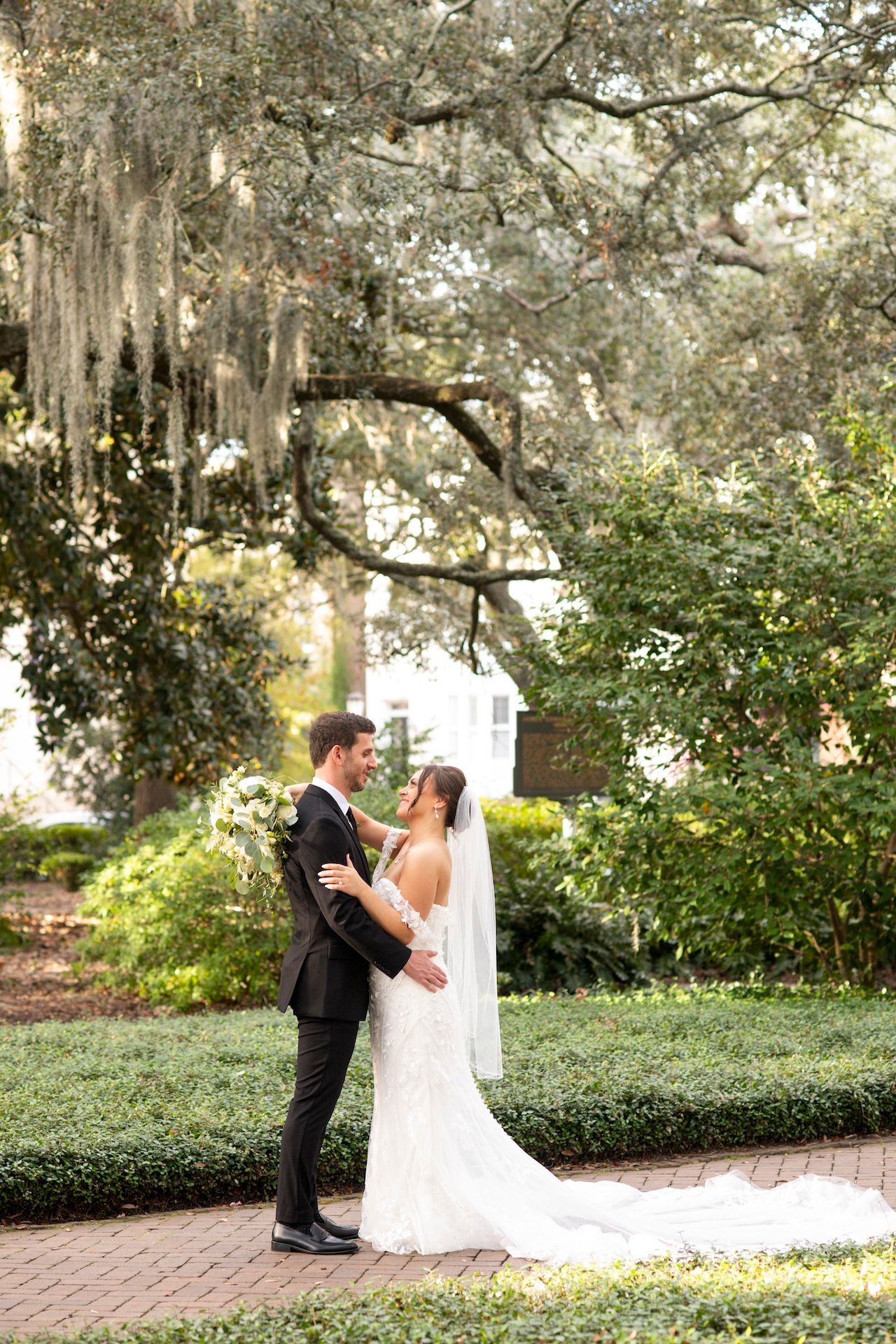 A romantic wedding photo series captured under Spanish moss-draped oak trees and brick pathways in a garden setting.