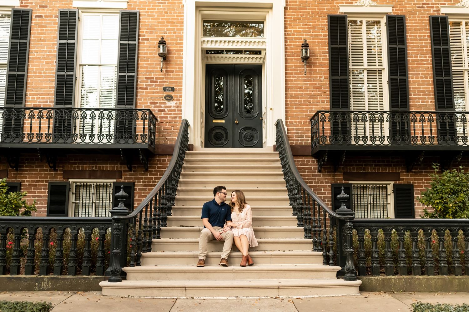 People sit on stone steps outside historic brownstone buildings along a tree-lined residential street in New York City.