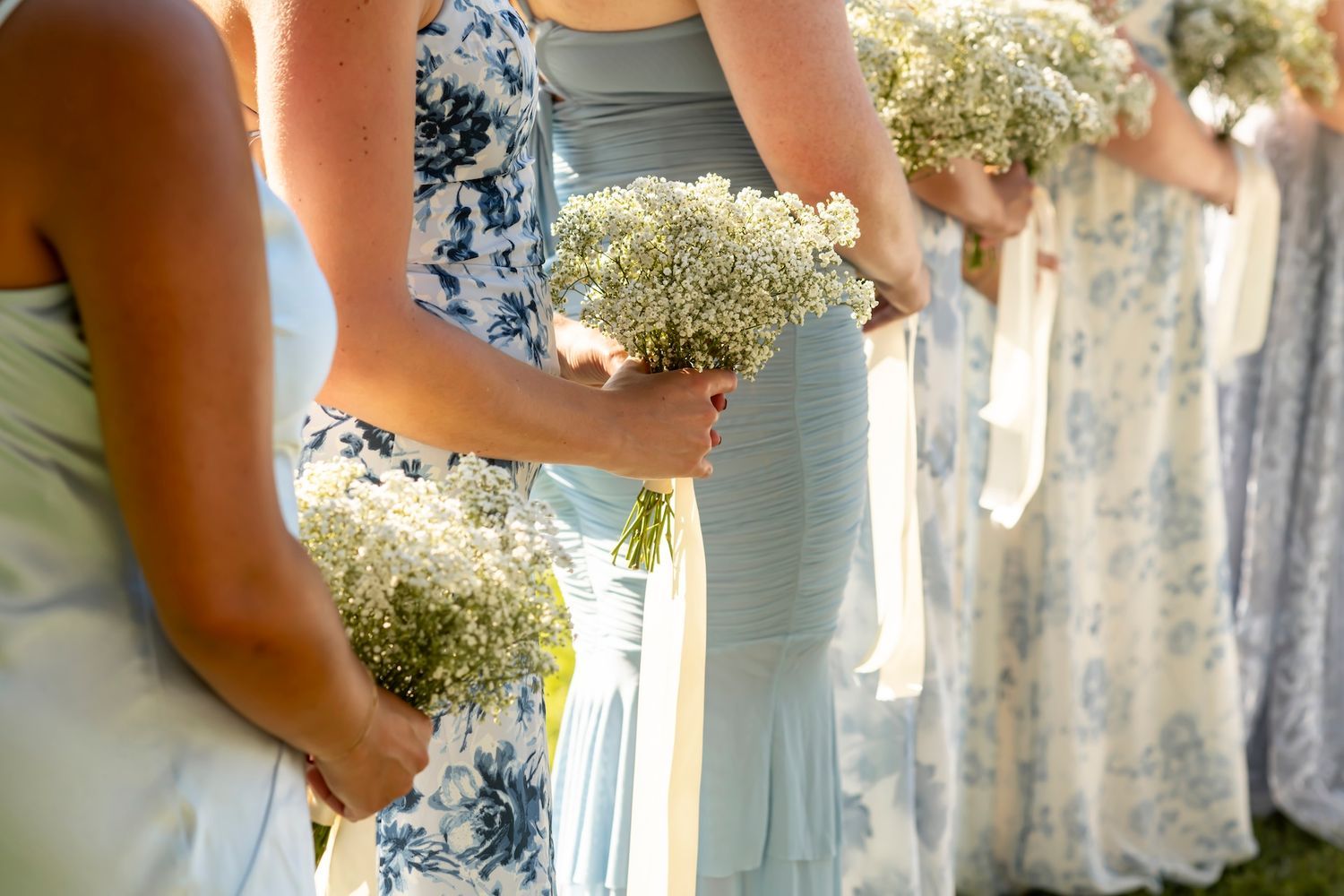 Bridesmaids in soft blue dresses hold delicate white baby's breath bouquets during a wedding ceremony.