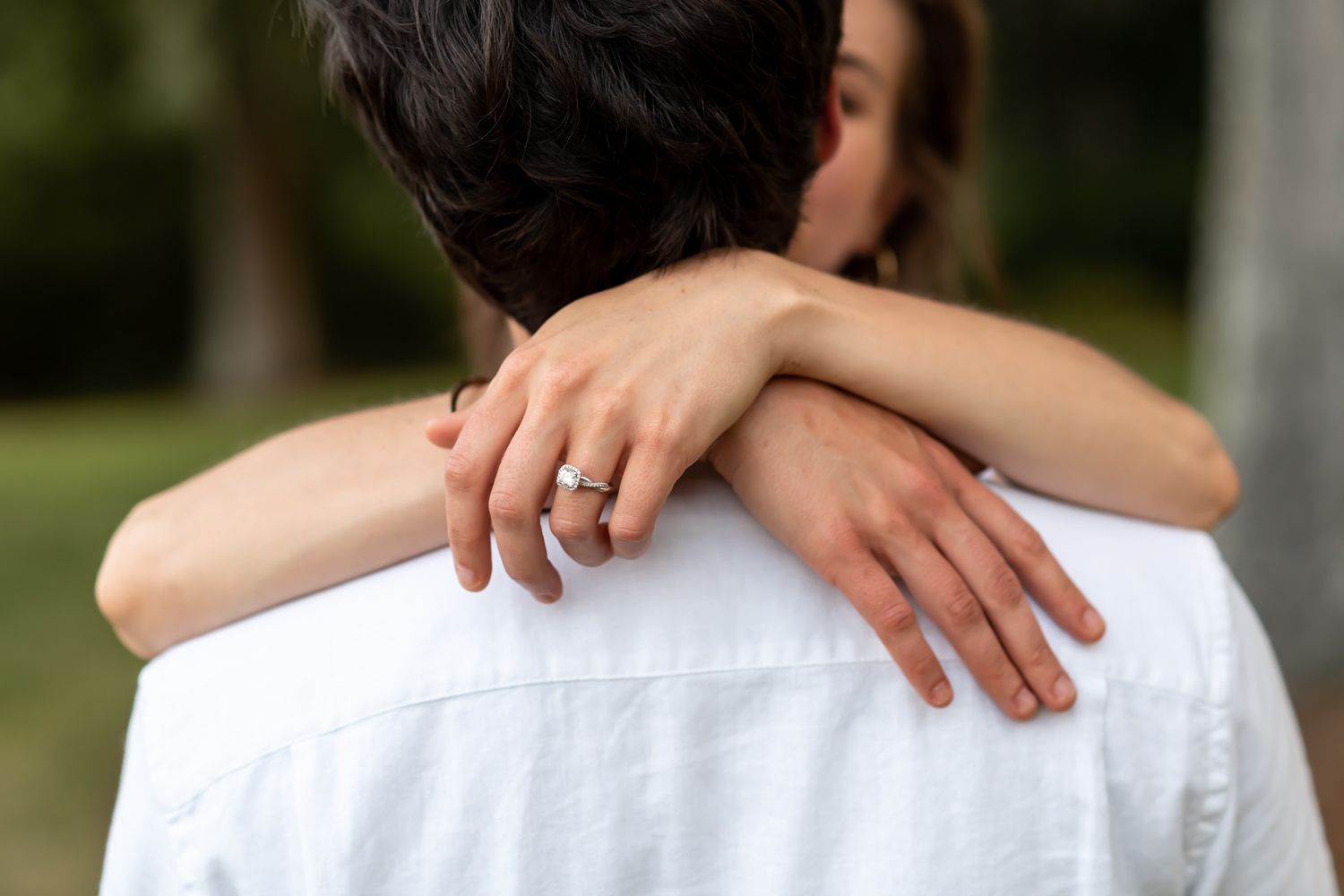 The hands of a couple in love gently hold each other while wearing white clothing at sunset.