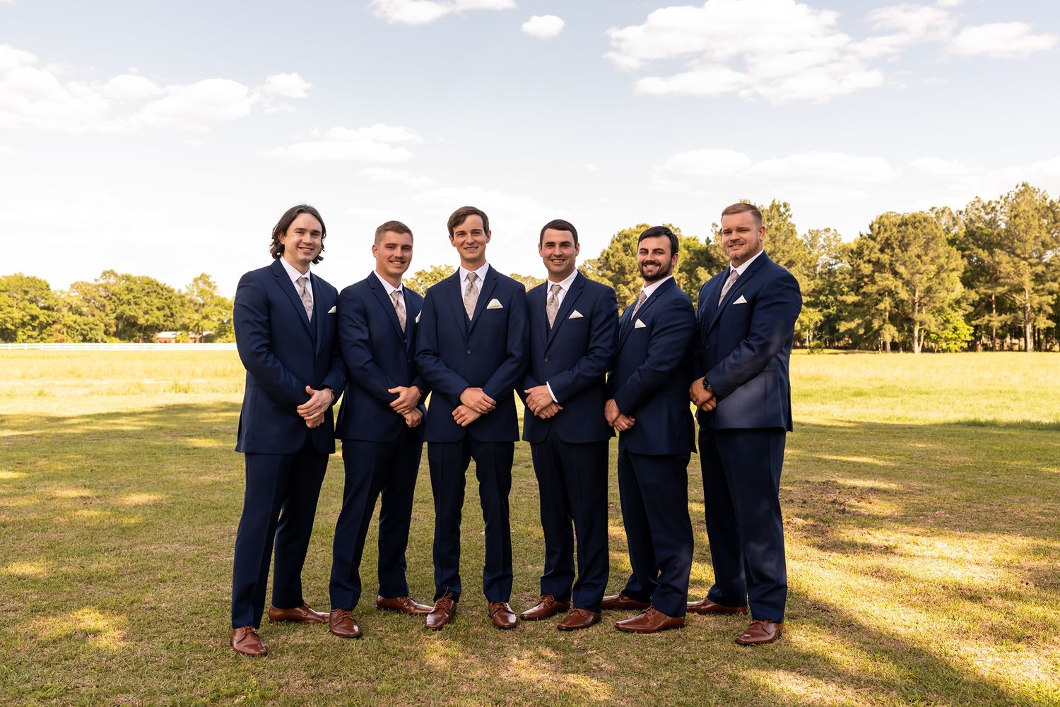 Groomsmen in navy suits pose together on a grassy hill during a wedding photoshoot at golden hour.