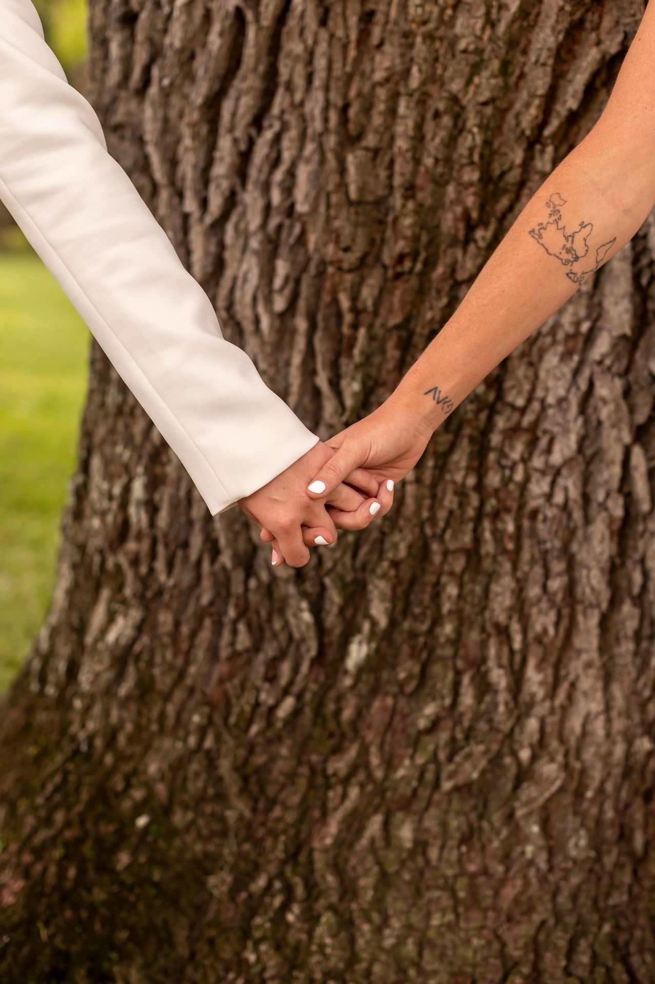 Close-up of two hands holding each other against a tree trunk background, with a visible tattoo on one arm.