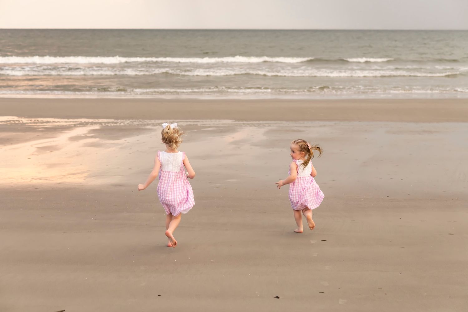 Two children in matching pink dresses dance together on a foggy beach at sunset.