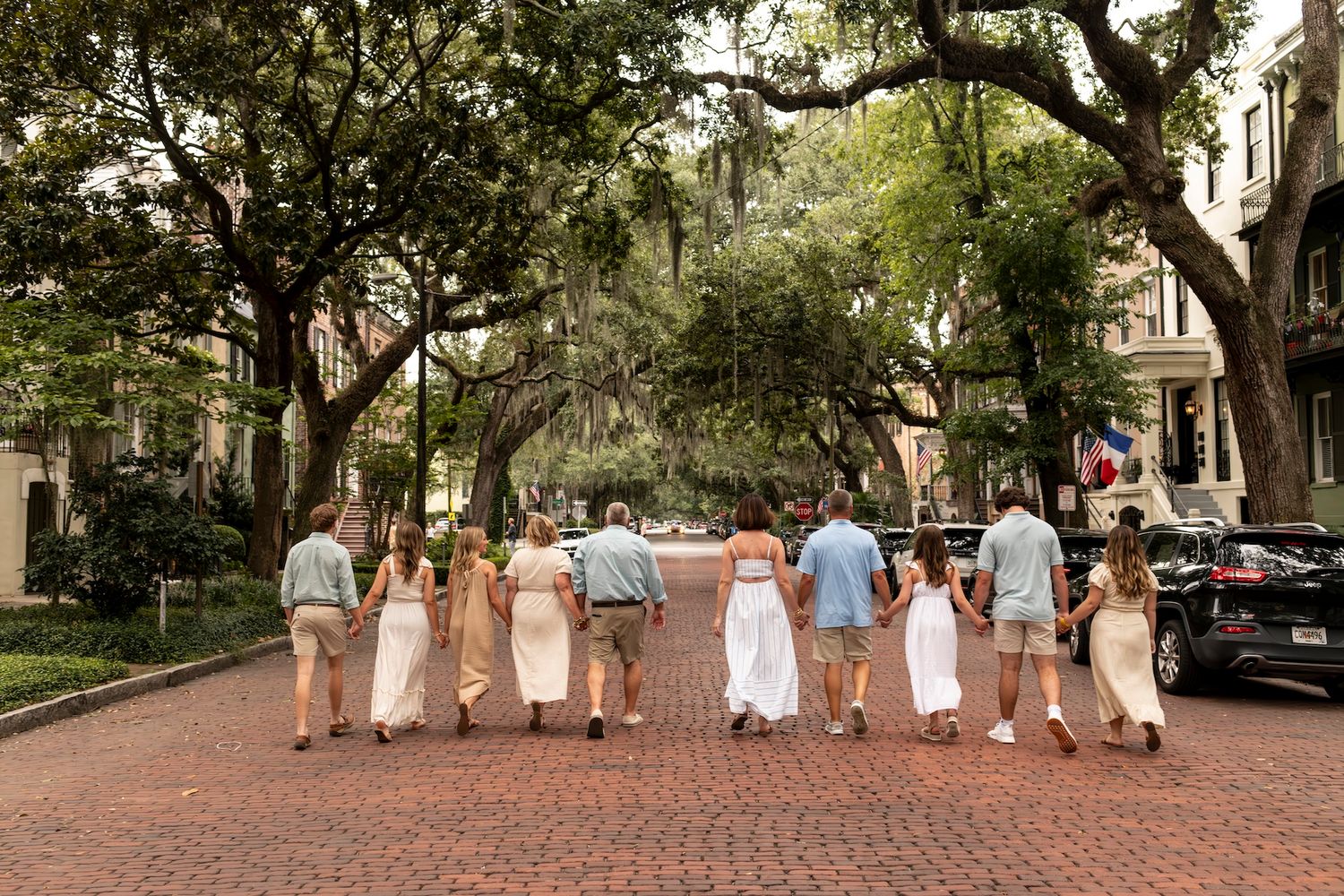 Wedding party walks down a tree-lined brick pathway in Savannah's historic district during golden hour.