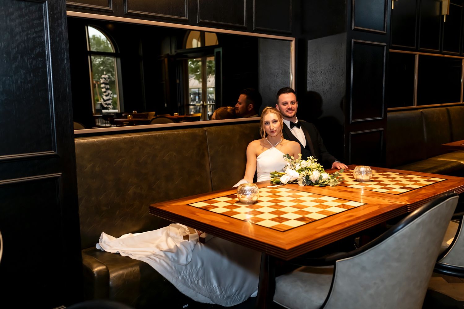 A couple shares an intimate moment at a wedding reception dinner table in a dimly lit restaurant setting.