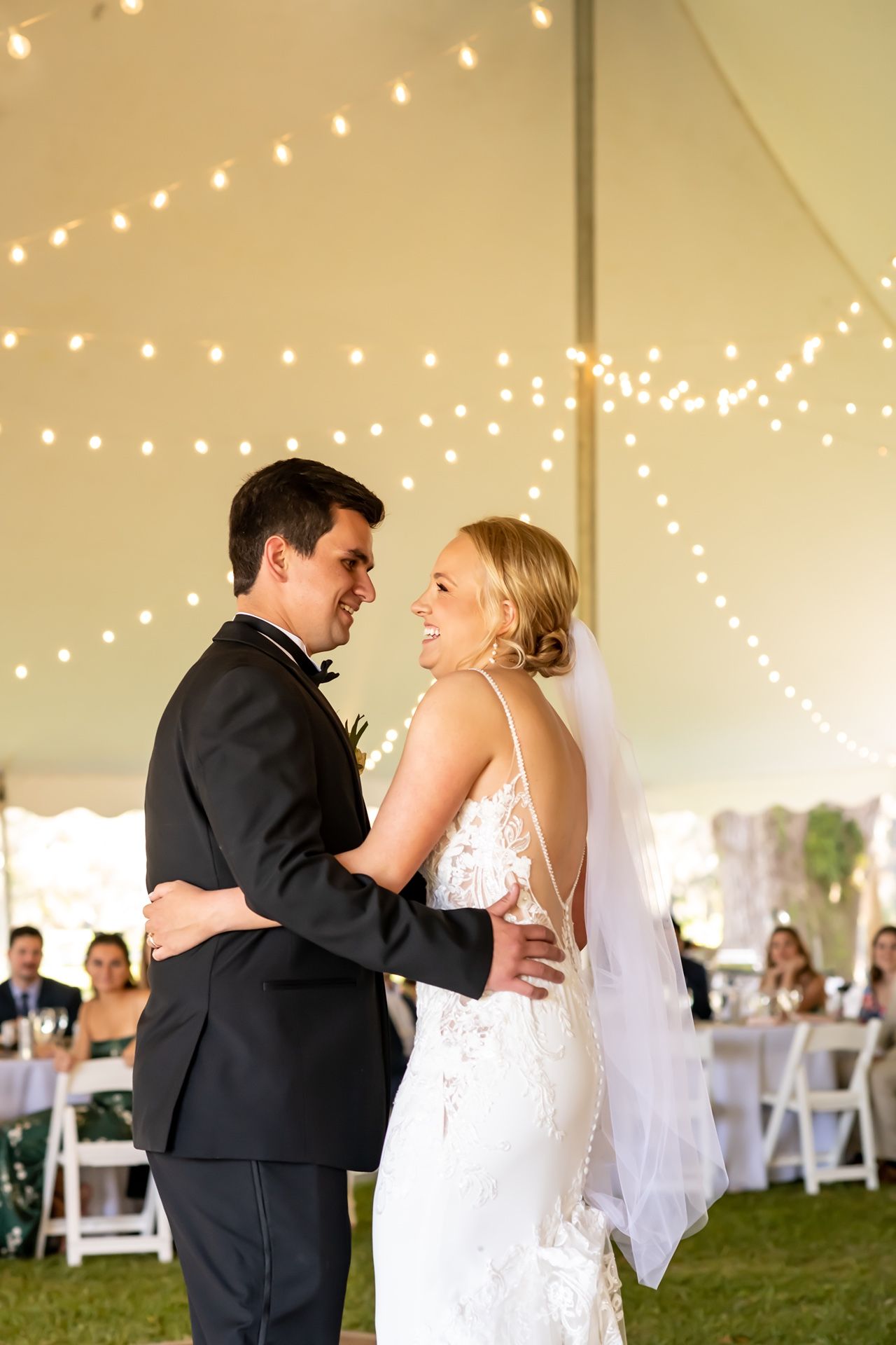 A first dance moment at a wedding reception under a tent with twinkling string lights creating a romantic atmosphere.