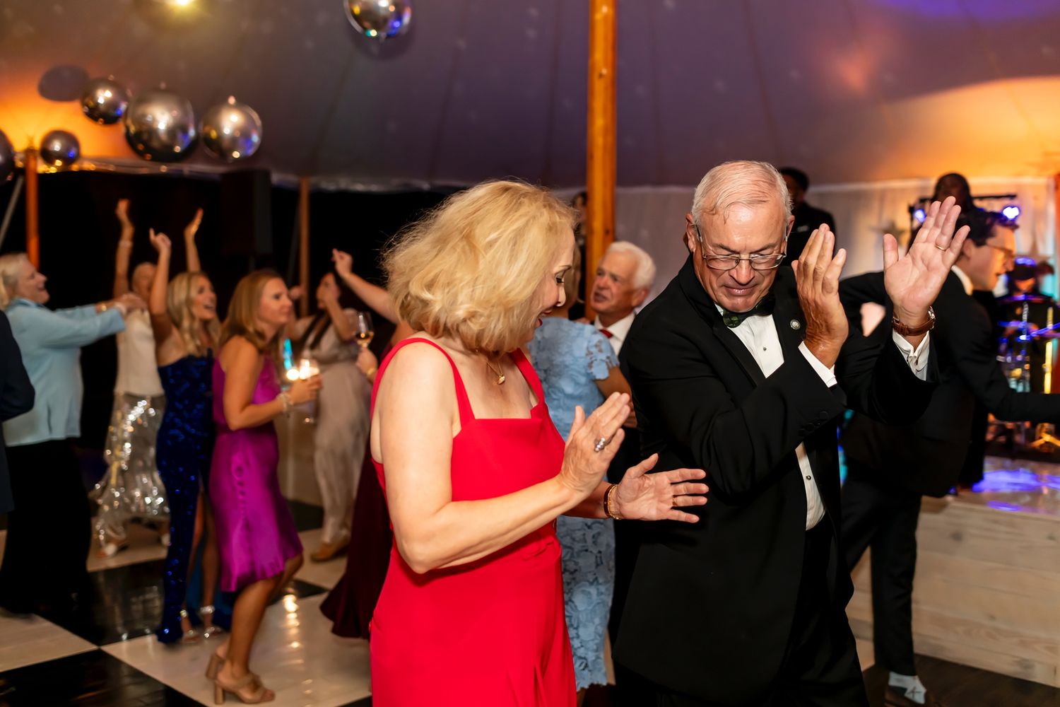 A group of individuals dancing together at a lively party with disco balls and warm lighting overhead.