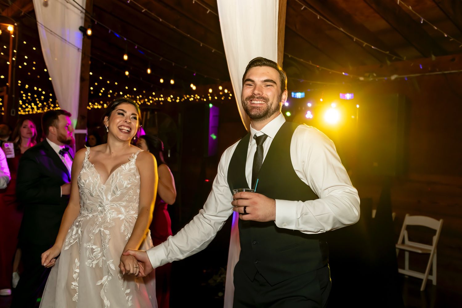 A couple celebrate and dance together at an evening wedding reception with sparkling lights in the background.