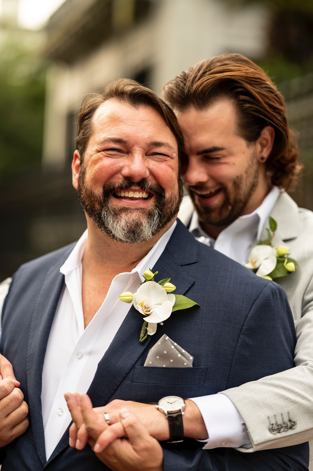 Two happy people in formal wedding attire sharing a joyful moment together, wearing boutonnieres and suits.