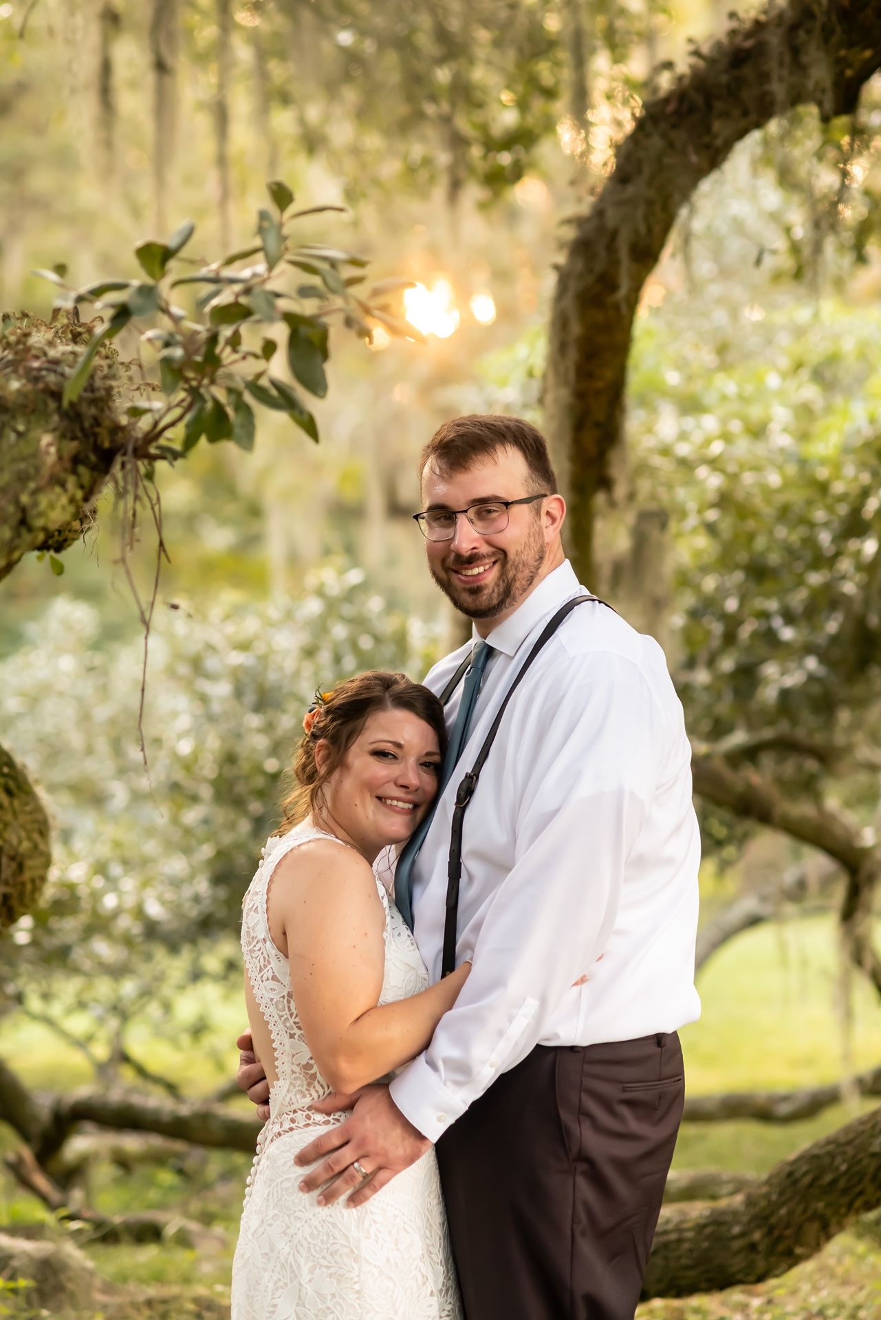 Couple shares romantic moments together in an outdoor setting with sunlit oak trees and Spanish moss in the background.