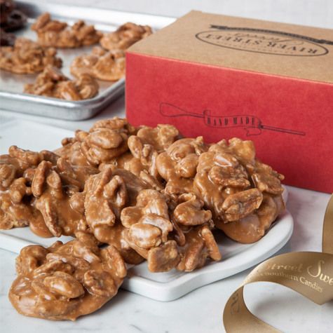 Golden pralines or nut clusters arranged on a white plate with a red gift box and gold ribbon in the background.