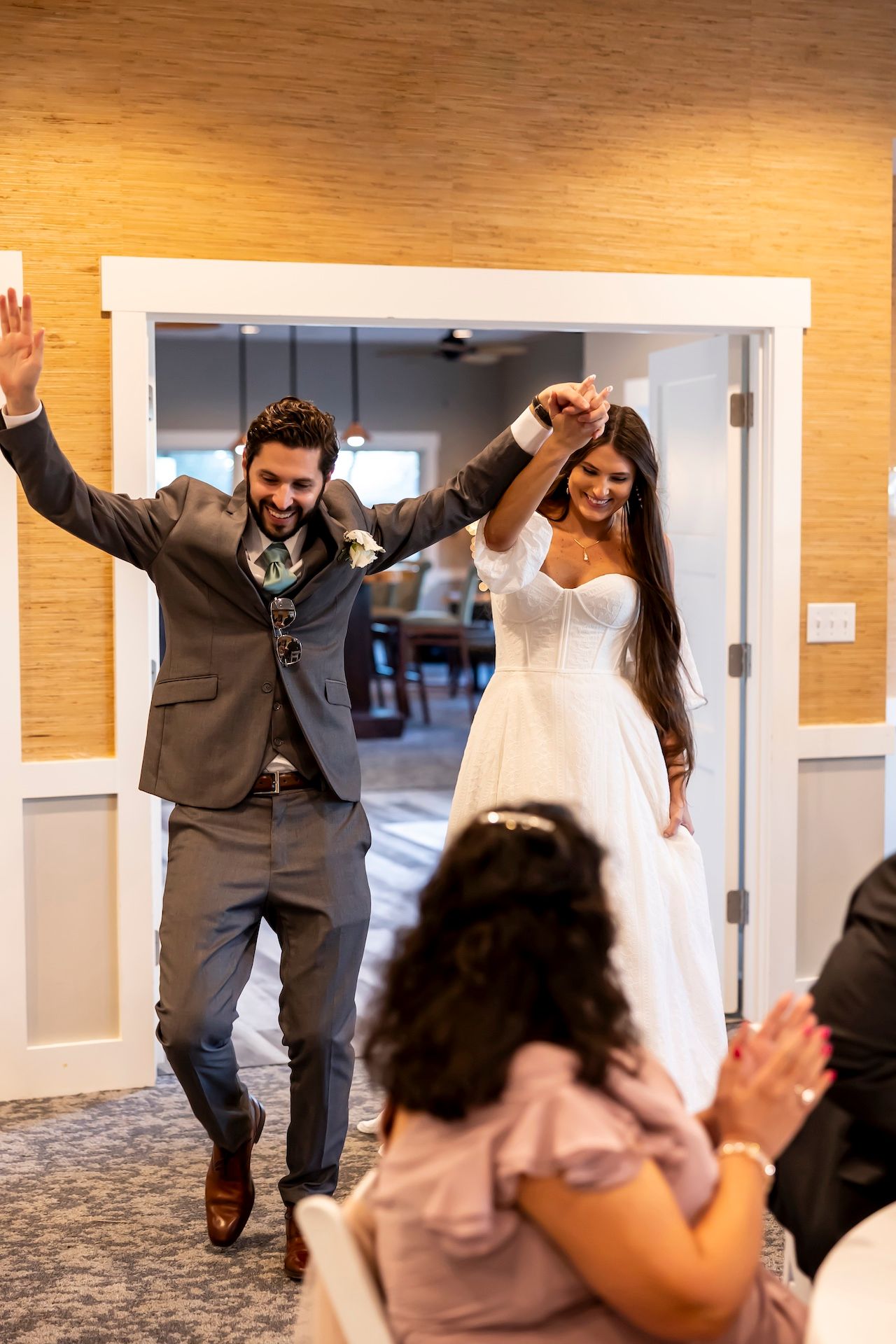 A joyful couple in wedding attire make their grand entrance with raised arms while guests cheer and celebrate.