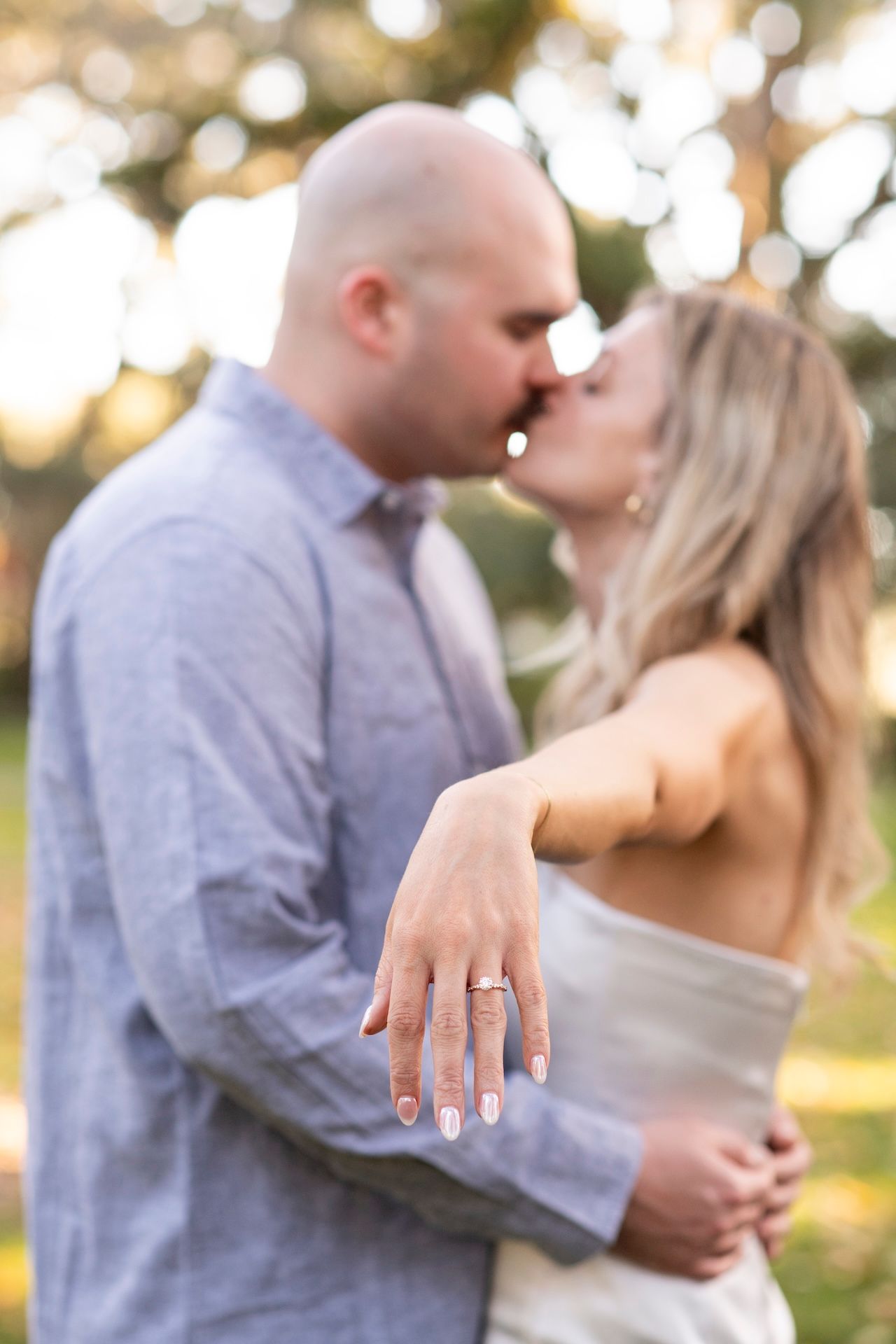 Close-up of an engagement ring on a bride's hand as couple shares intimate moment in outdoor setting during sunset.