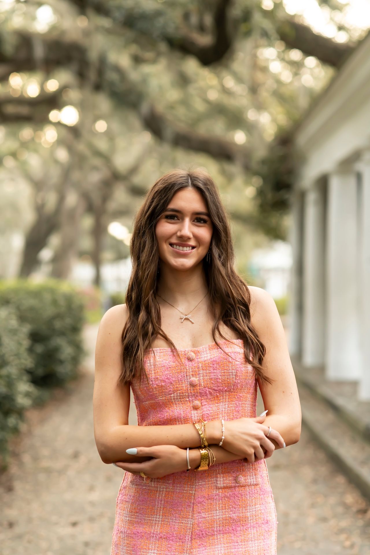 A person in a pink plaid sundress poses on a tree-lined path with bokeh lighting in the background.