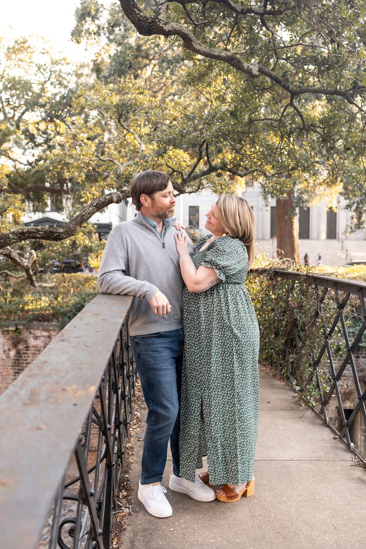 A couple shares an intimate moment on a historic iron bridge surrounded by autumn trees.
