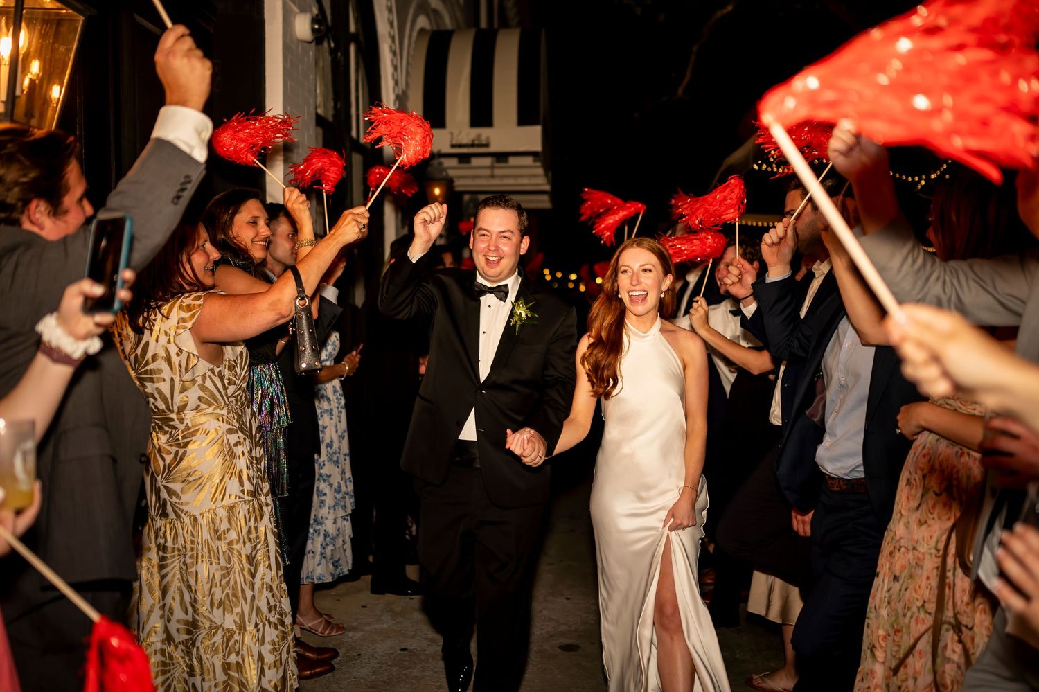 Wedding guests dance and celebrate under red decor at an elegant evening reception party with a festive atmosphere.