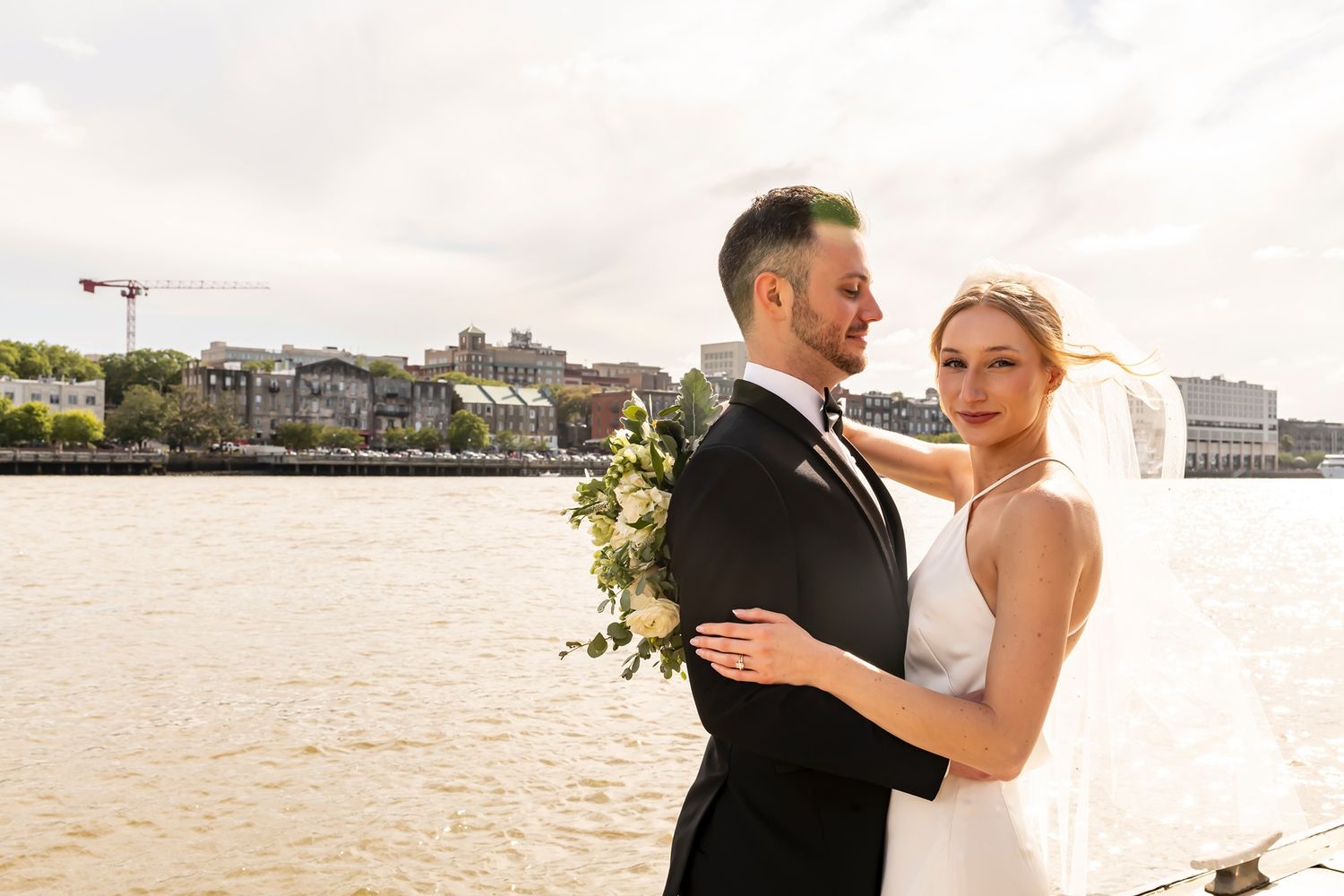 Newlyweds share a romantic moment while dancing together on a dock by the waterfront at sunset.