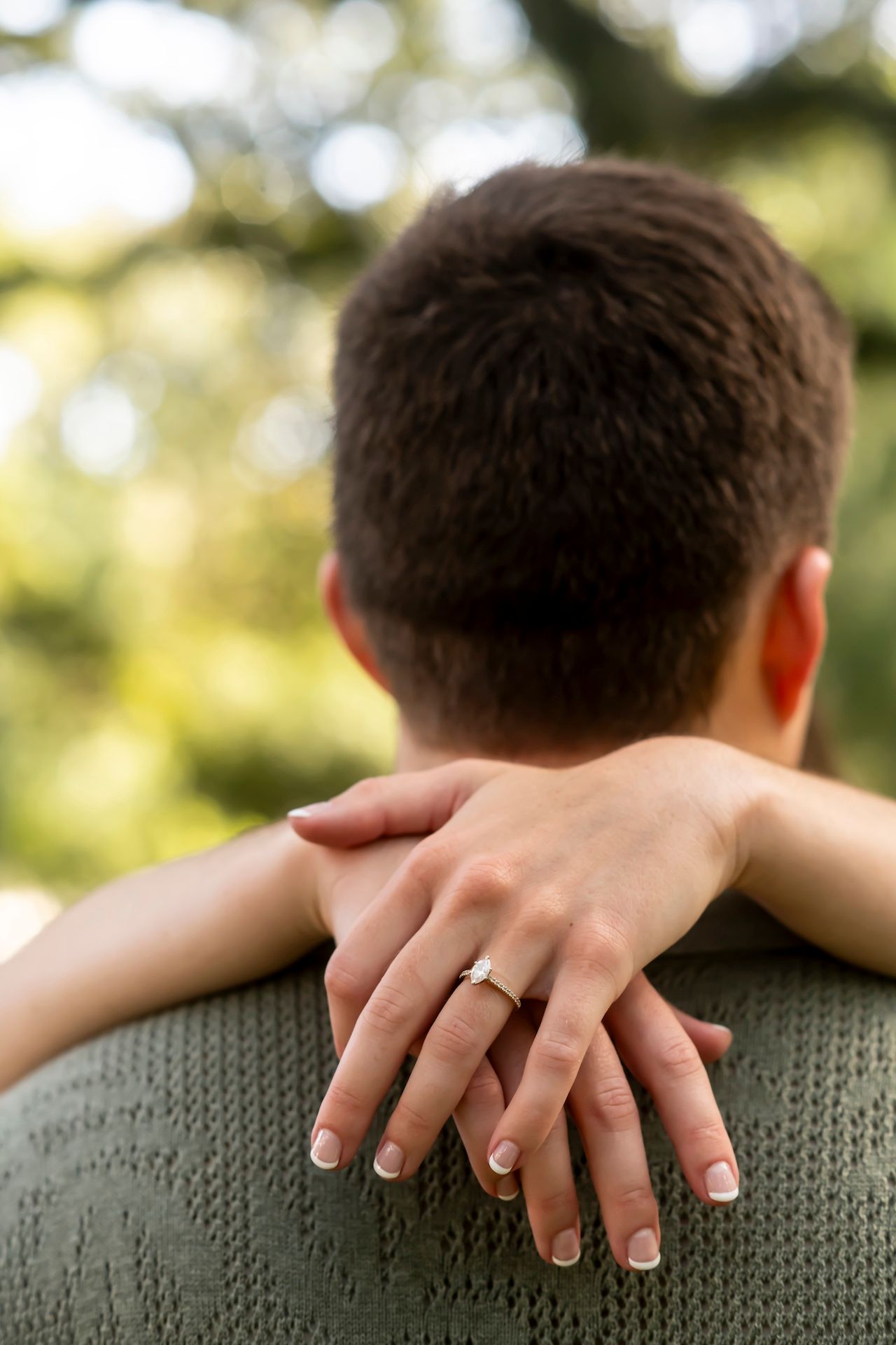 Close-up view of hands resting on a grey knit sweater showing a wedding ring against a soft bokeh background.