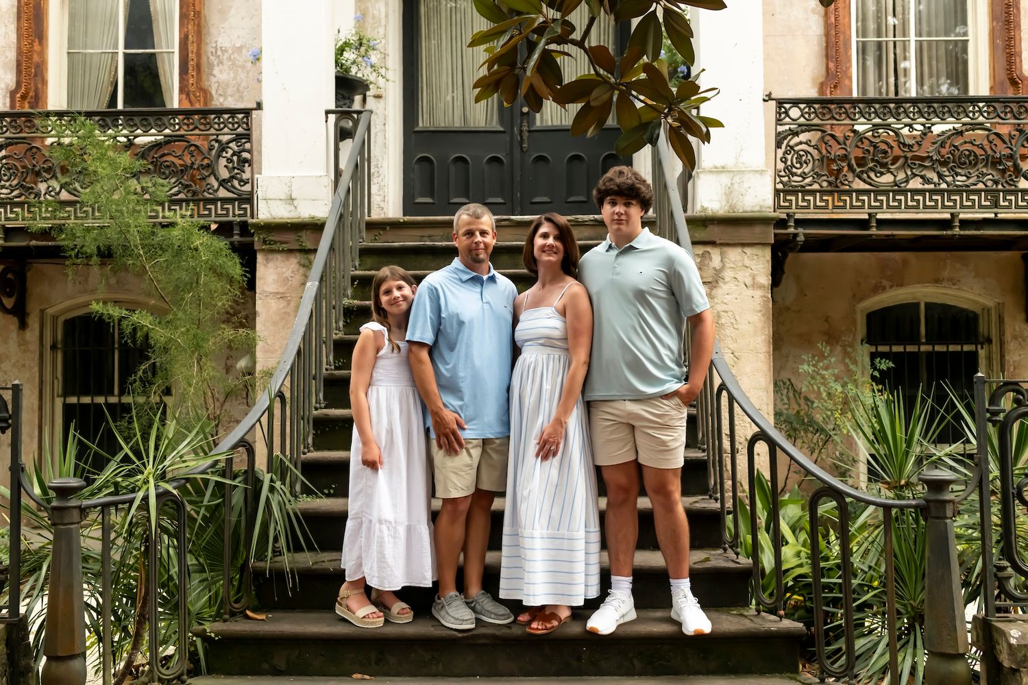 Group standing on historic brick stairs with ornate iron railings and greenery outside a traditional building in Charleston.