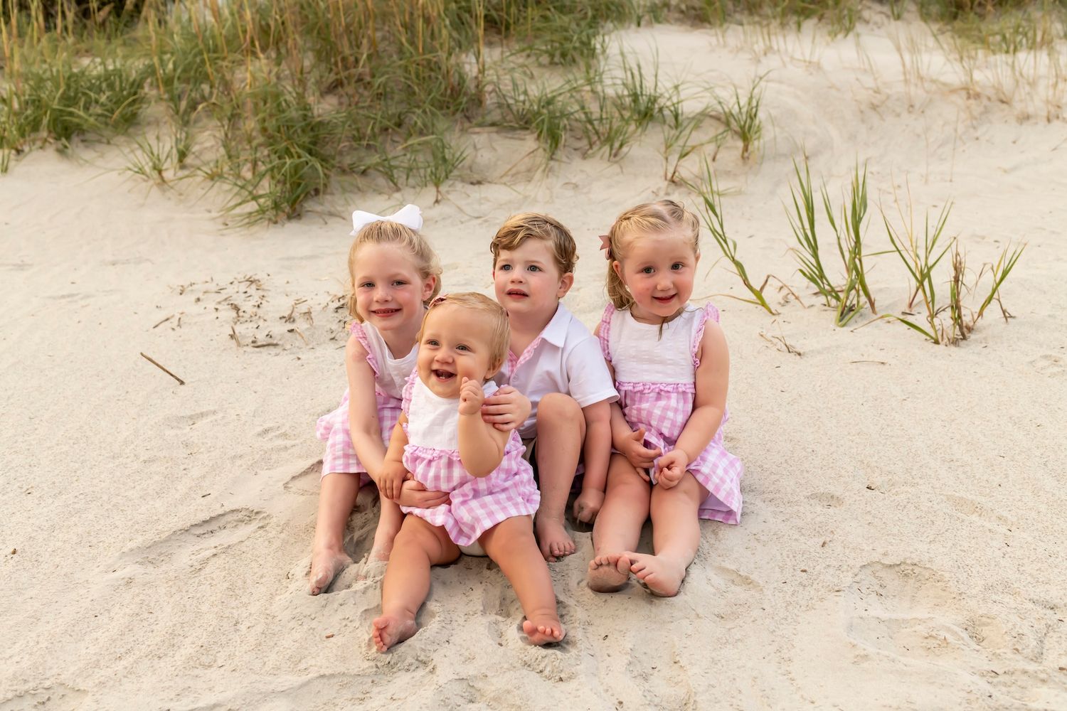 Group of children wearing coordinating pink outfits playing and laughing together on sandy beach.