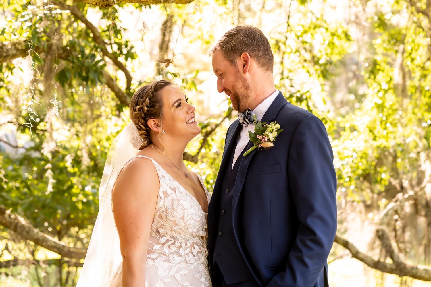 Happy bride and groom sharing a joyful moment together in a sunlit garden setting with natural foliage backdrop.