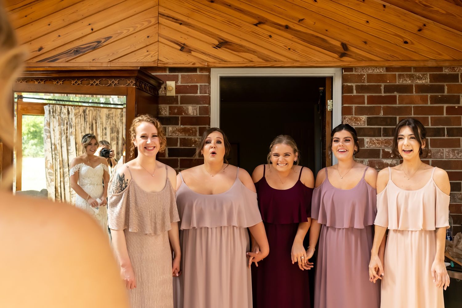 Group of bridesmaids in matching pale lavender dresses standing in a row outside a brick building.
