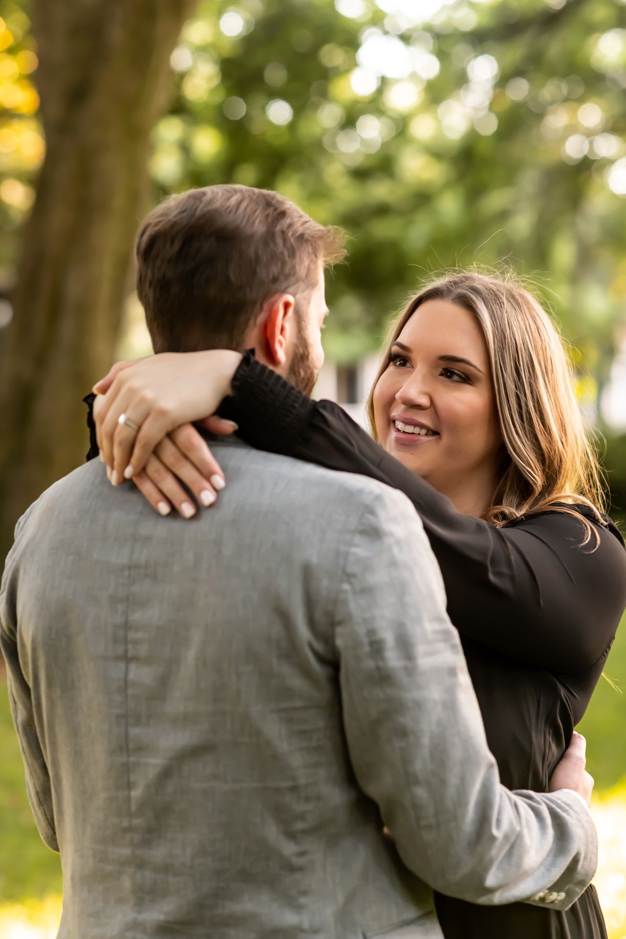 A couple embraces outdoors with soft bokeh lighting and trees in the background during a romantic moment.