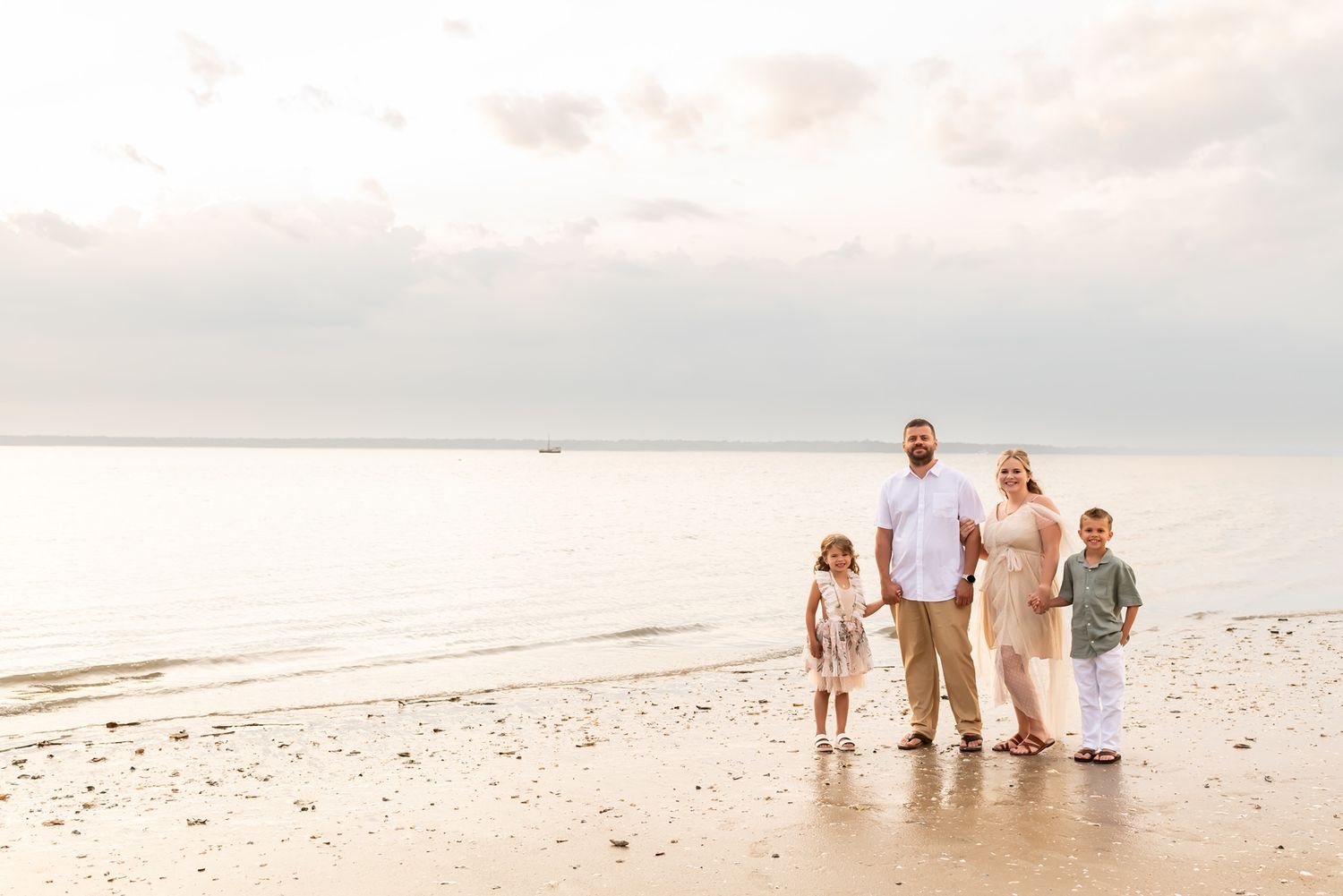 A group of people wearing light colored clothing stand together on a sandy beach at sunset.