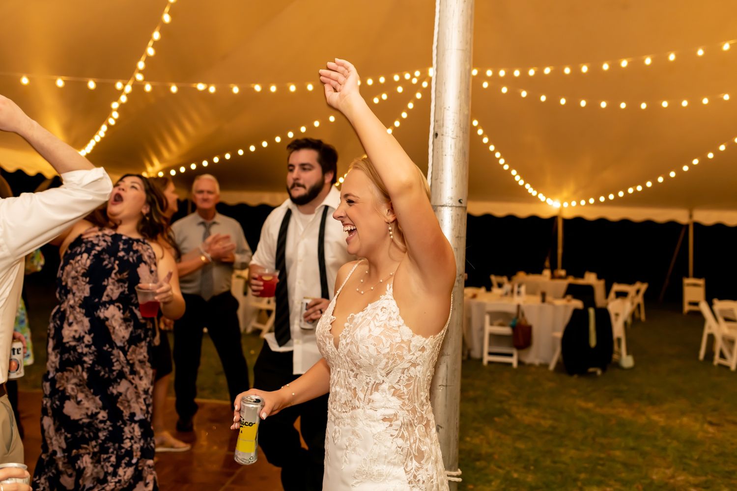 Couples dance beneath twinkling string lights at an outdoor evening wedding reception under a white tent.
