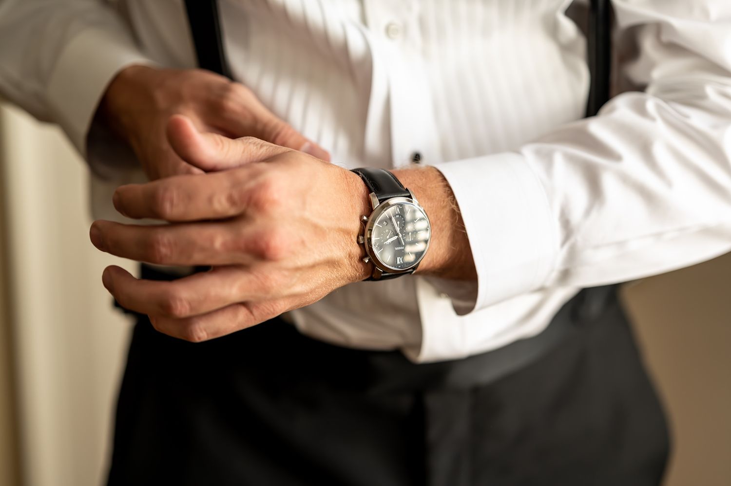 Close-up view of hands adjusting an elegant silver wristwatch worn with crisp white dress shirt sleeves.