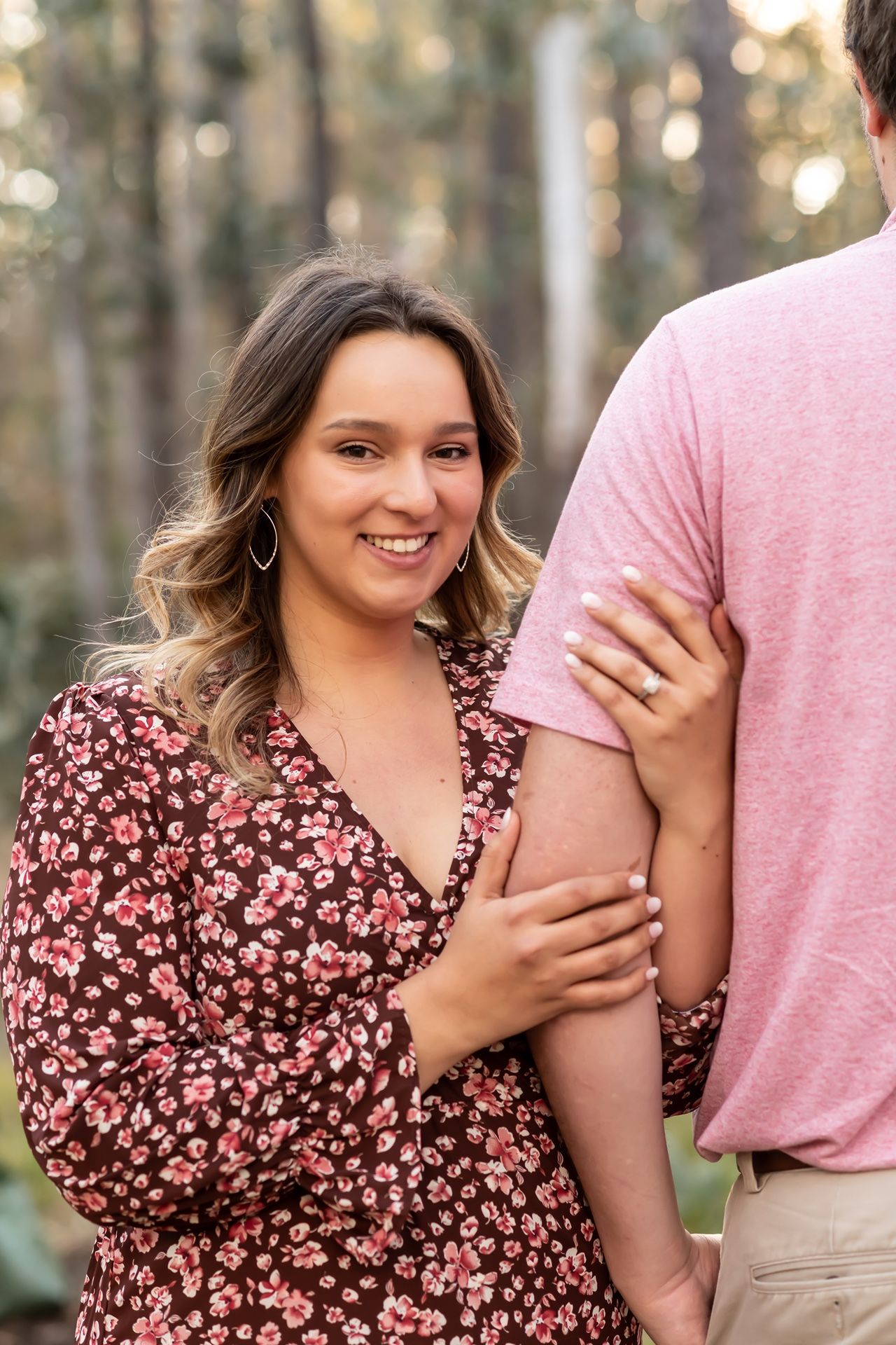A couple in casual attire embraces during a photo session in a wooded area with natural lighting.