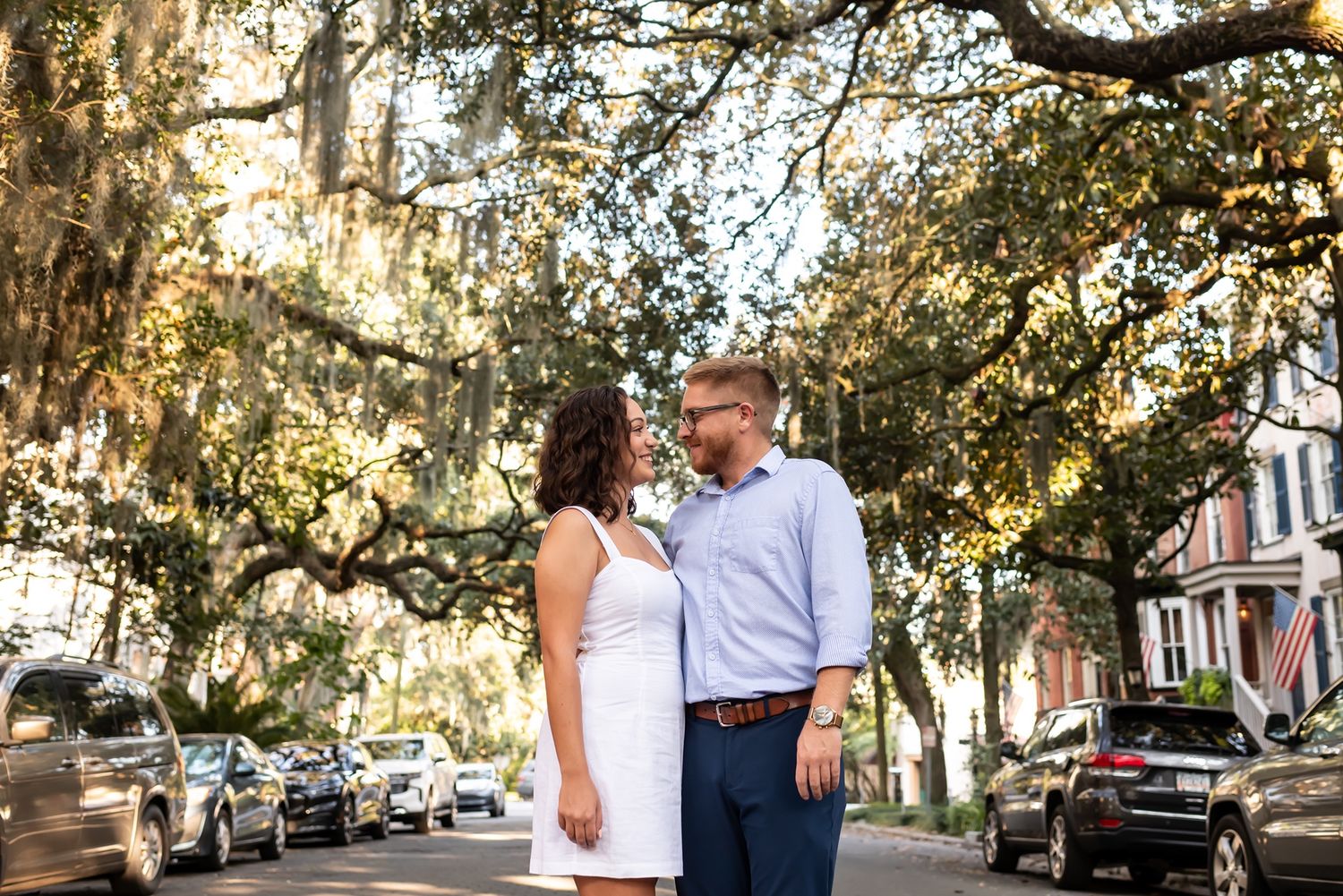 A couple embraces on a tree-lined street during a golden sunset engagement photoshoot.