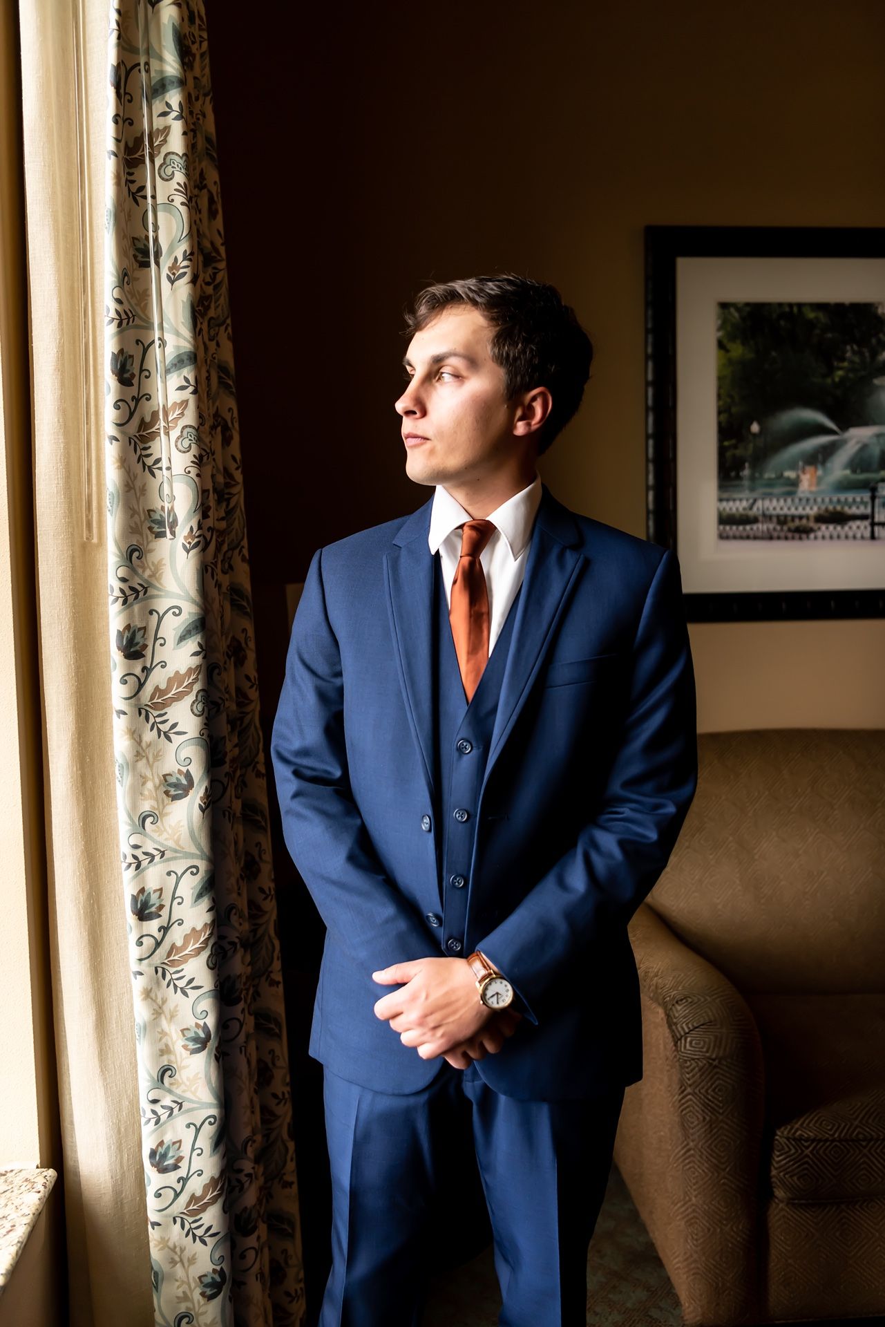 Elegantly dressed person in navy blue suit gazes through window light in atmospheric photography sequence.