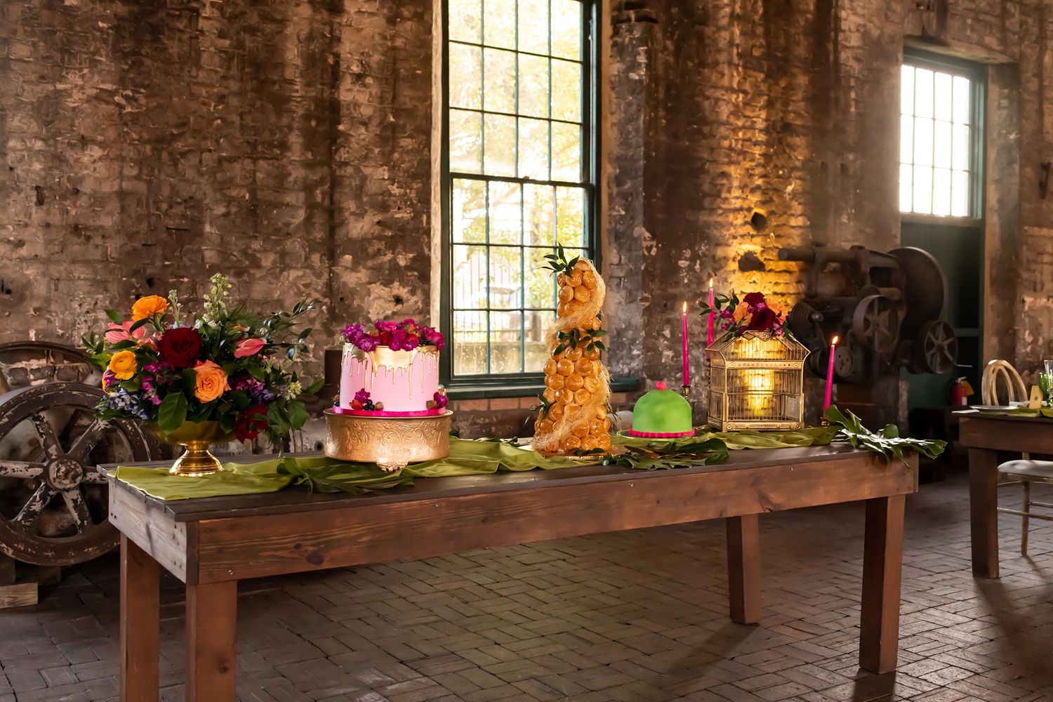 A rustic wooden table displays colorful floral arrangements and lanterns in a brick-walled room with natural window light.