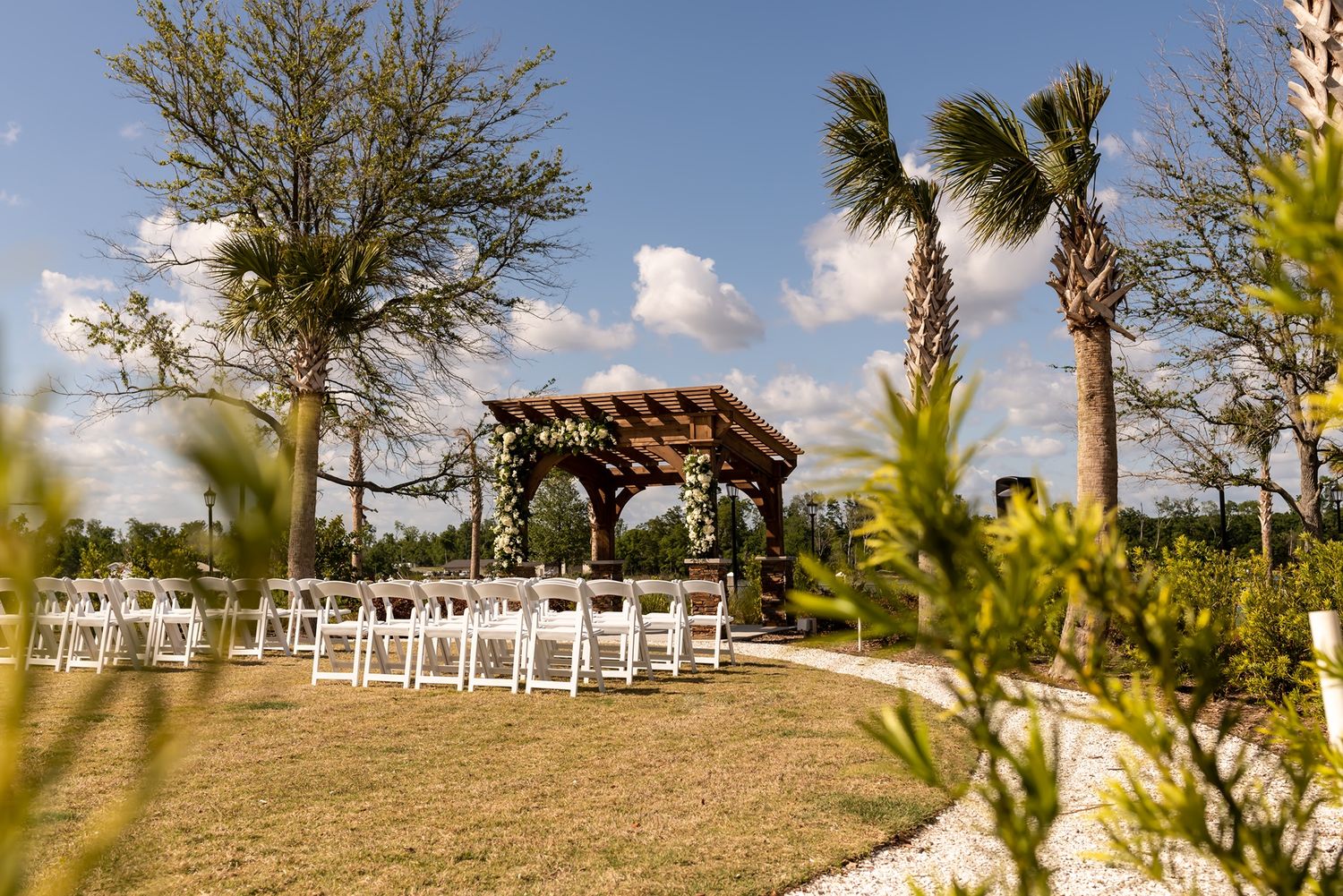 White garden chairs arranged at a scenic outdoor wedding venue surrounded by palm trees and clear blue skies.